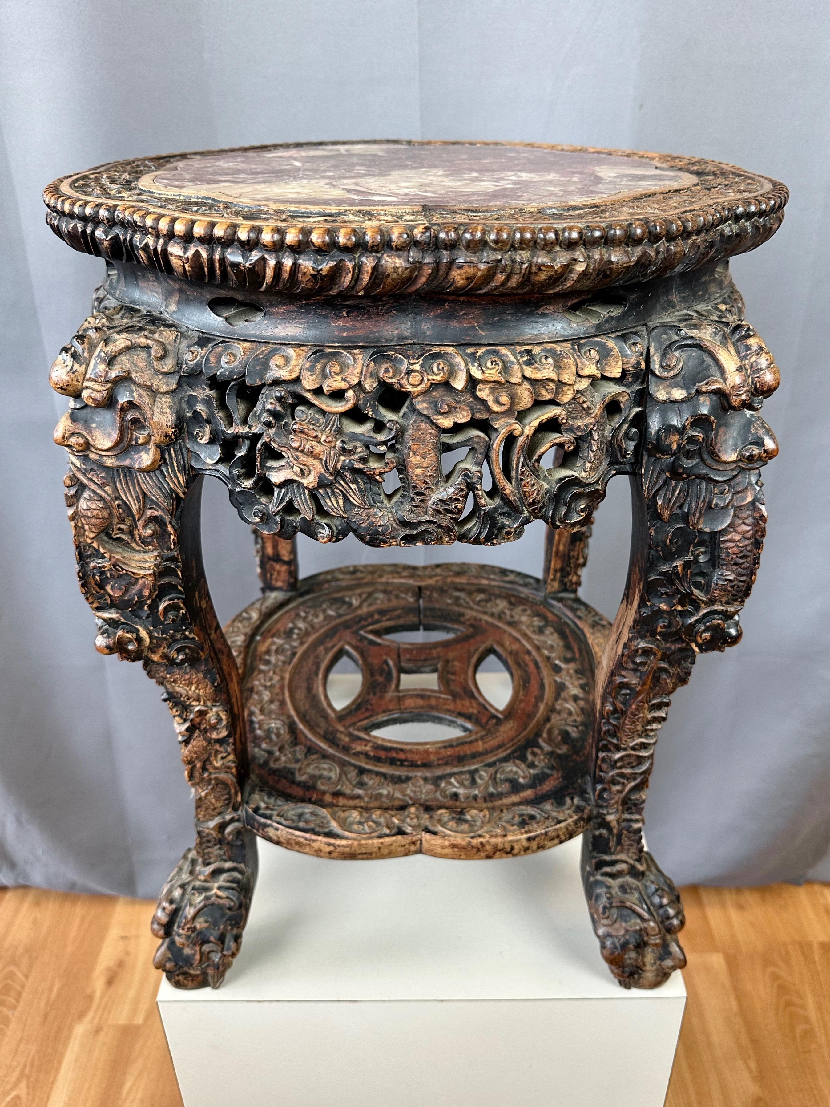A mid-19th century Chinese Qing dynasty era dragon and coin motif ebonized hand-carved elm and marble two-tier taboret. Perfectly sized and suited to serve as a side table upon which to display a lamp, vase, art object, or plant.

Features a