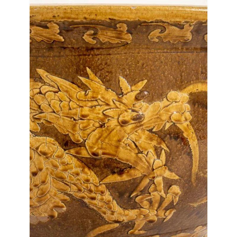 Eine chinesische glasierte ockerfarbene Keramik-Jardiniere mit einem Flachrelief, das zwei fünfzackige Drachen um den Übertopf herum zeigt.  Der Topf ist breit und kann eine große Pflanze oder einen Baum aufnehmen.
