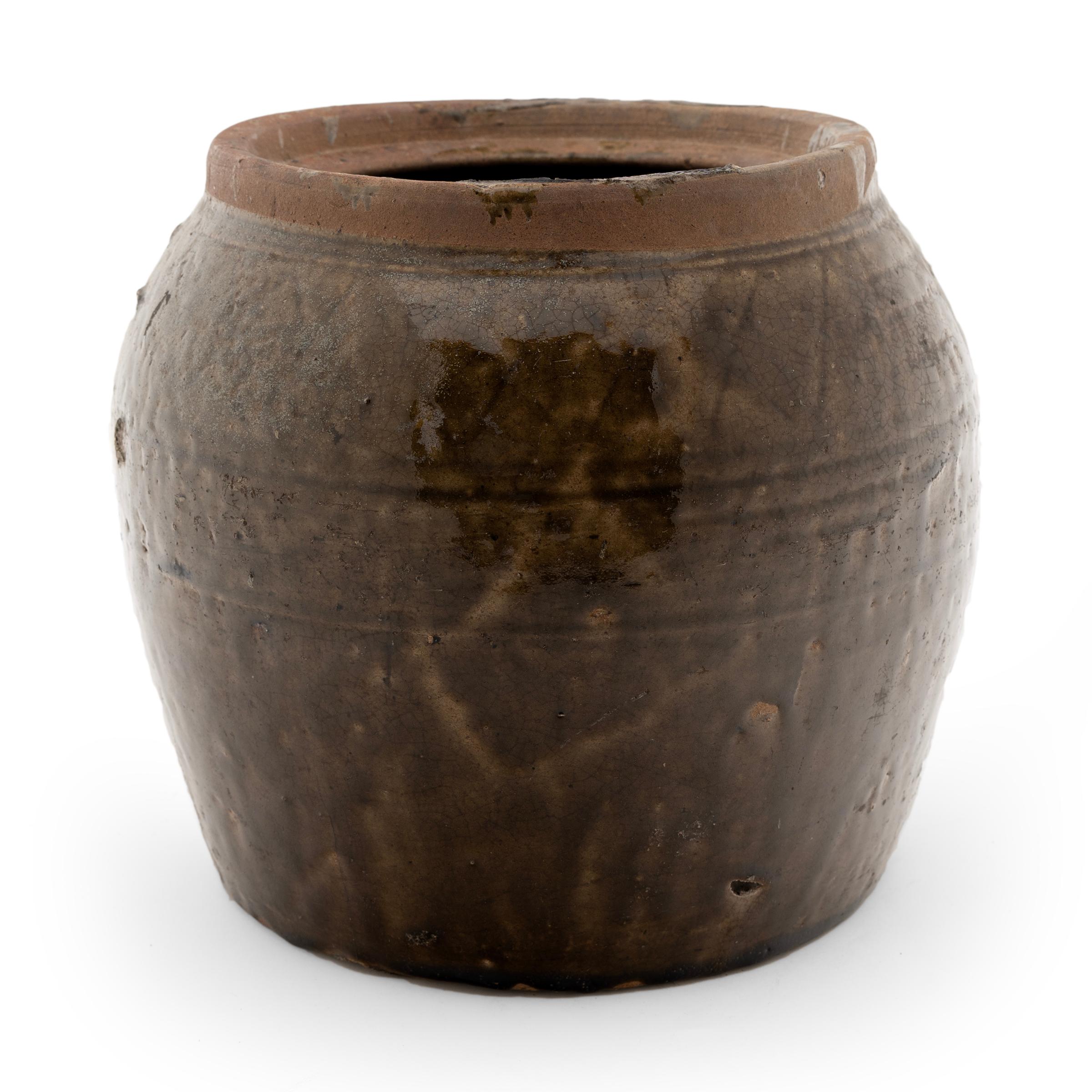 A captivating textured glaze coats the simple, slightly-tapered form of this Qing-dynasty kitchen jar. Drip patterns and firing imperfections give the jar fantastic character, casting shades of light and dark brown across the vessel. Crafted in the