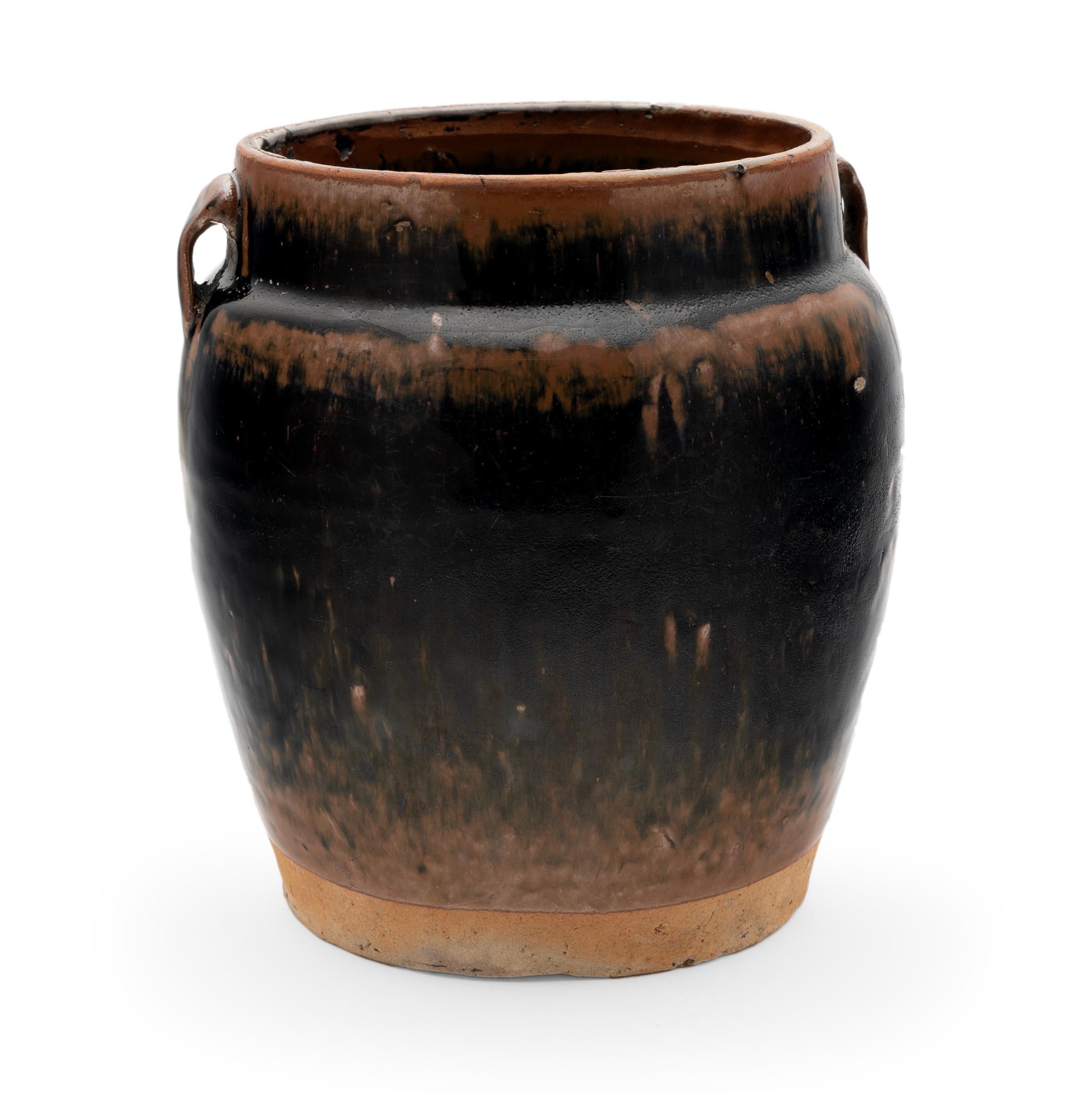 A thin dark glaze clings to the gentle swell of this 19th-century jar, exhibiting a rich range of tonal color. The wide-mouth jar was once used to store food or condiments in a Qing-dynasty kitchen, as evidenced by its interior glaze. Stopping short