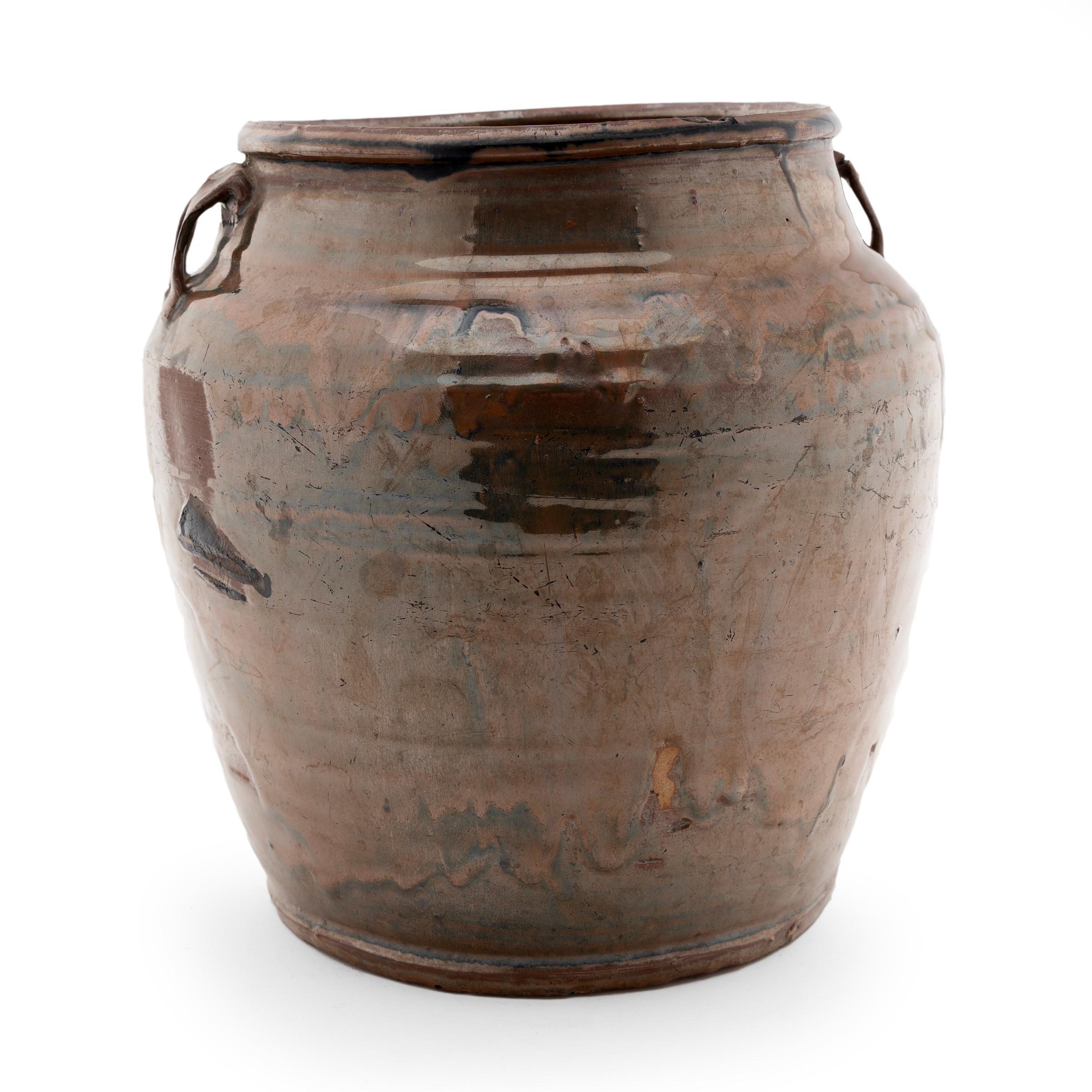 Coated inside and out with a rich drip glaze, this early 20th century jar was originally used for storing foods and condiments in a Provincial Chinese kitchen. The wide-mouth jar has a slightly tapered form with rounded shoulders, two