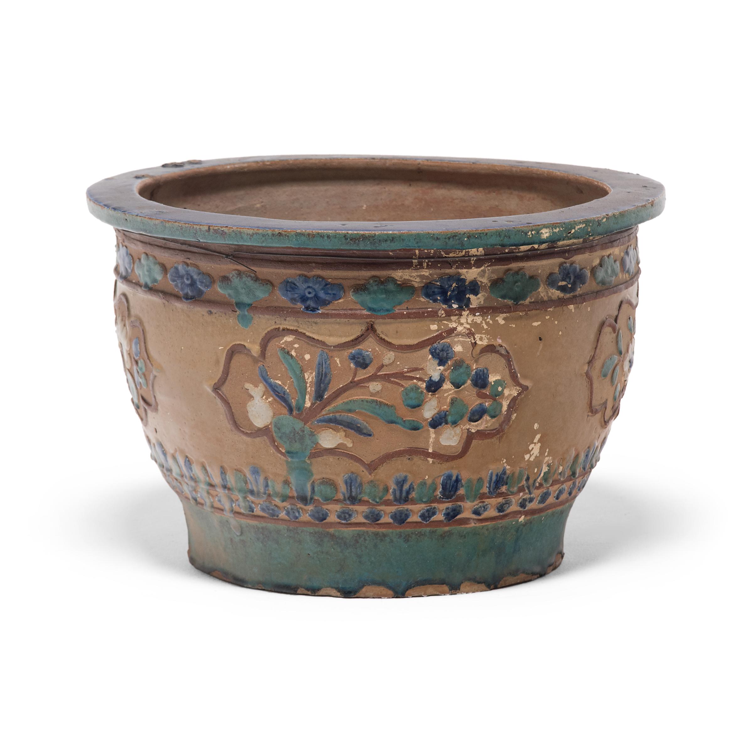 This lovely ceramic planter dates to the early 20th century and features low relief decoration colored by blue, green, and light brown overglaze. The basin has a footed base, a flat lip, and rounded sides patterned with bands of simple floral motifs