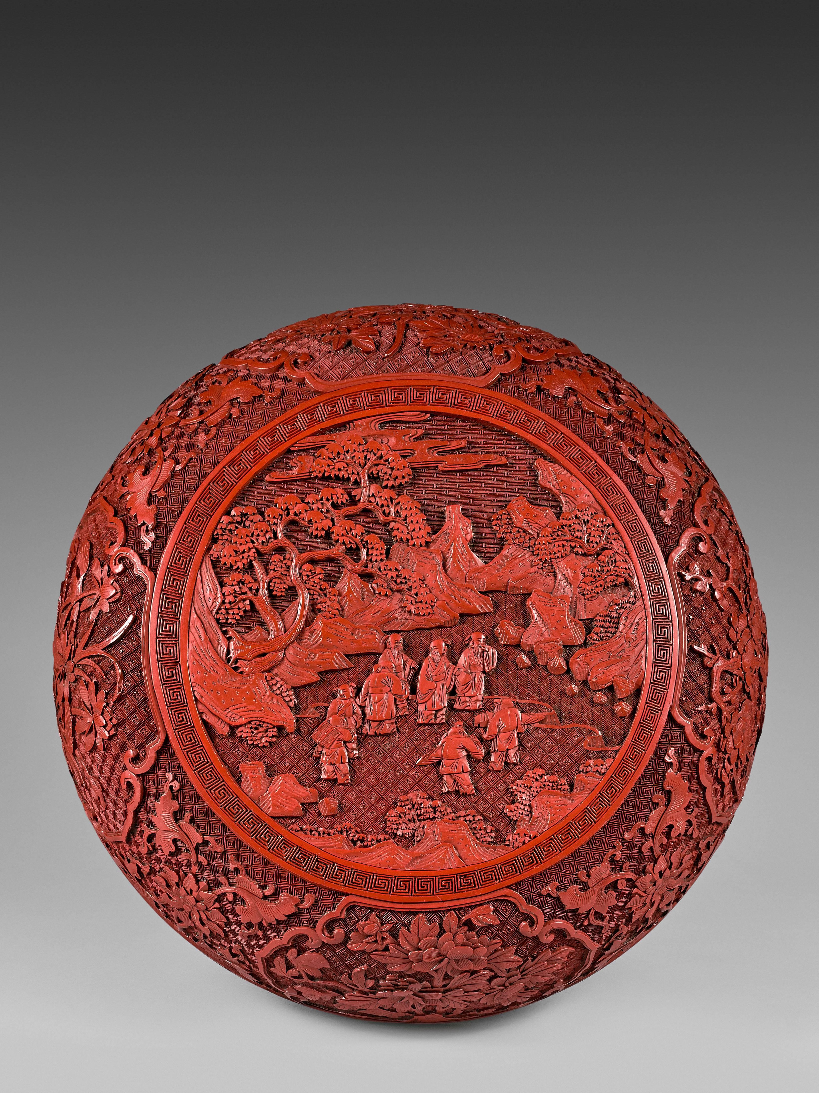 The round shape box resting on a small feet with keyfret pattern. The cover adorned with a round medallion depicting scholars and their servants in a rocky landscape. The sides of the box and cover with multilobed cartouches enclosing flowers of the