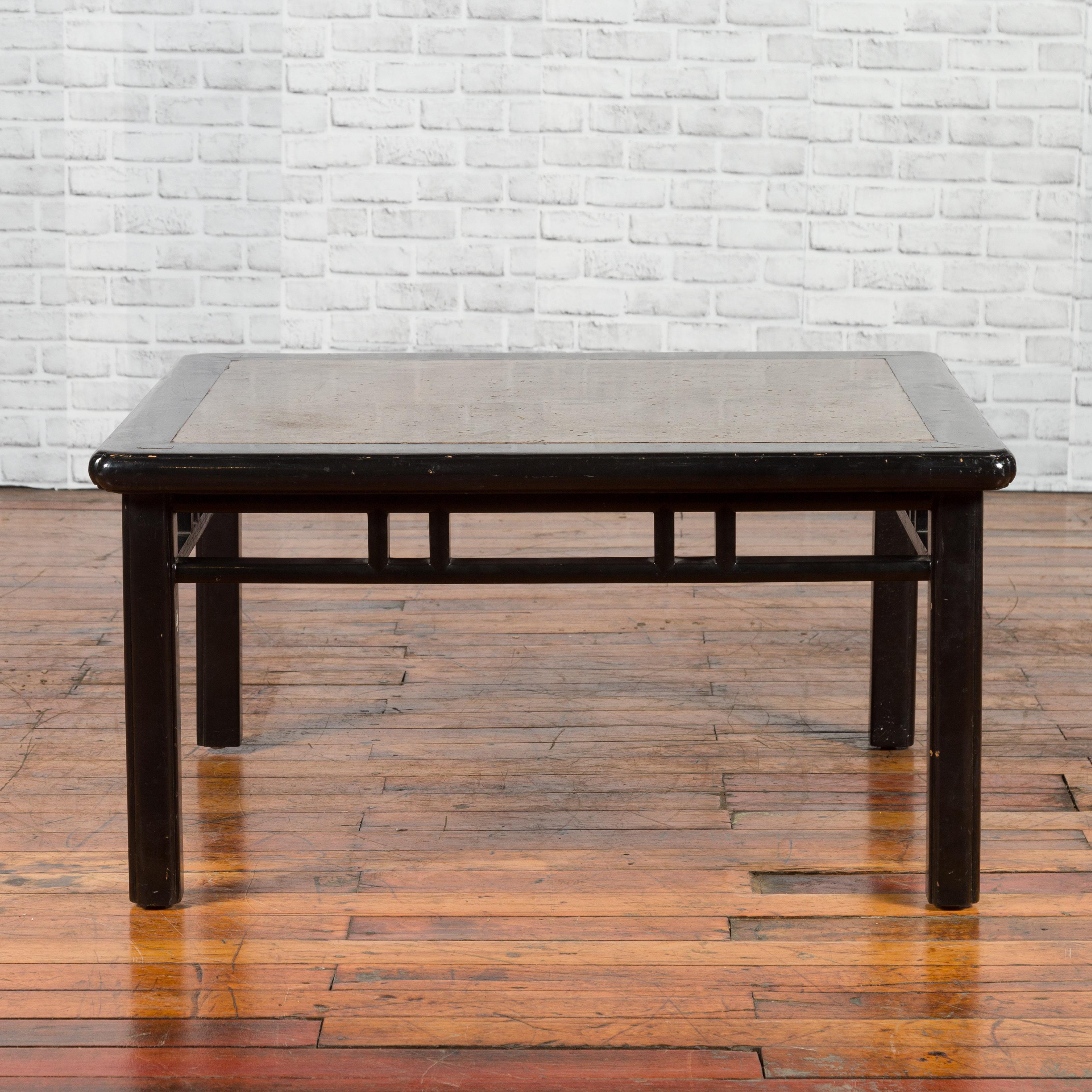 A Chinese black lacquered coffee table from the early 20th century, with stone top. Created in China during the early years of the 20th century, this black lacquered coffee table features a square variegated stone inset top sitting above an open