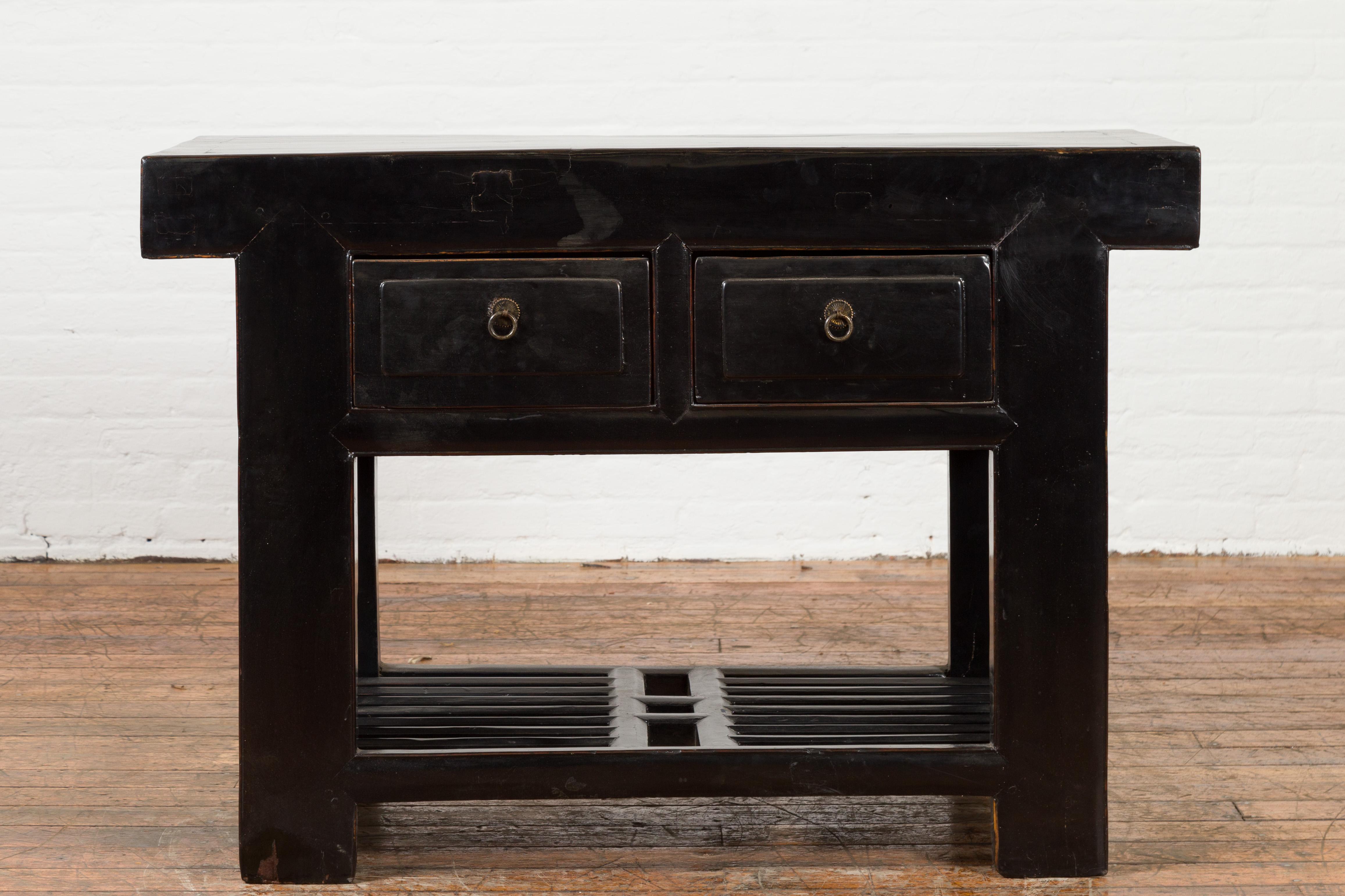 A Chinese black lacquered table from the early 20th century, with two drawers and open slatted shelf. Created in China during the early years of the 20th century, this console table features a rectangular top with central board, sitting above two