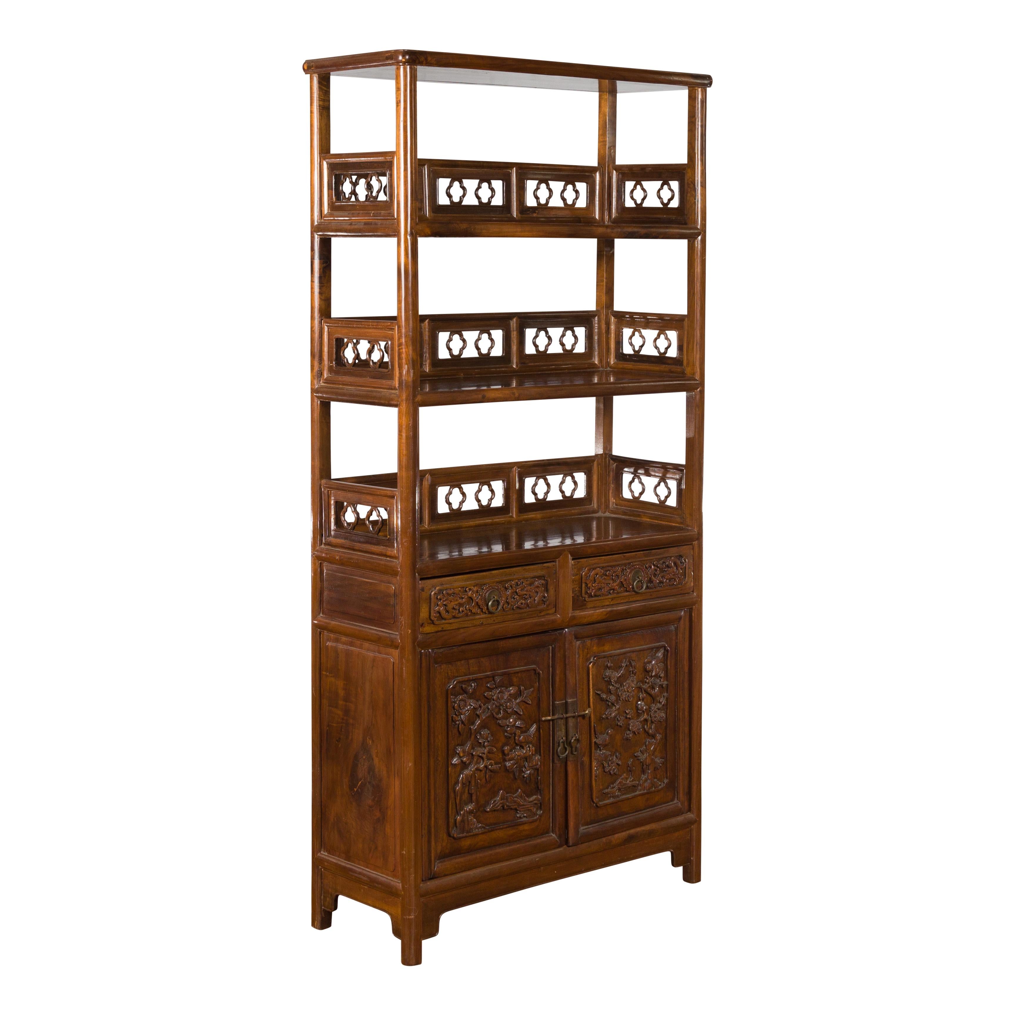 A Chinese bookcase from the early 20th century, with carved open shelves, two drawers and lower cabinet. Created in China during the early years of the 20th century, this bookcase features carved open shelves adorned on three sides with pierced