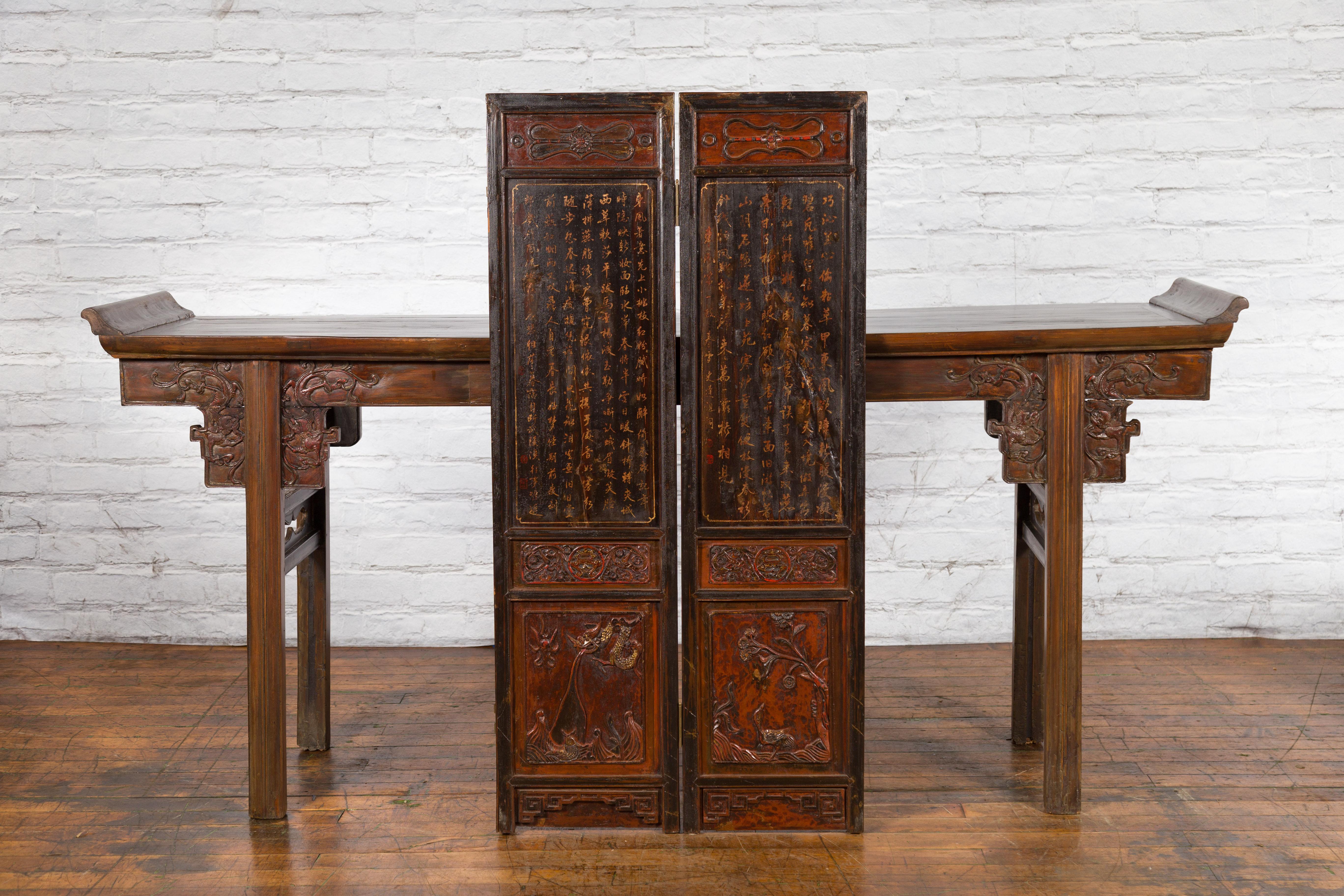 A Chinese two-panel screen from the early 20th century, with carvings, gilt motifs and calligraphy. Created in China during the early years of the 20th century, this screen features a brown lacquered ground accented with dark red highlights and