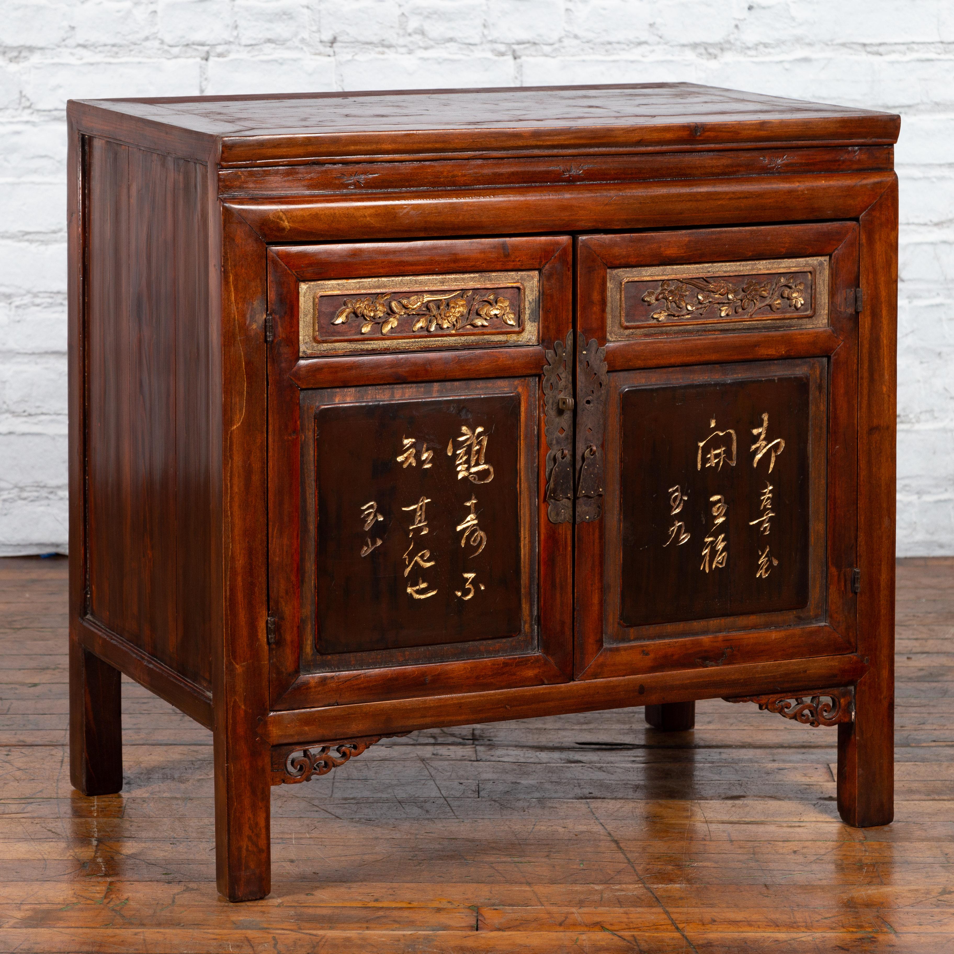 A Chinese antique cabinet from the early 20th century, with gilded calligraphy and carved floral motifs. Created in China during the early years of the 20th century, this cabinet features a rectangular top with central board, sitting above a