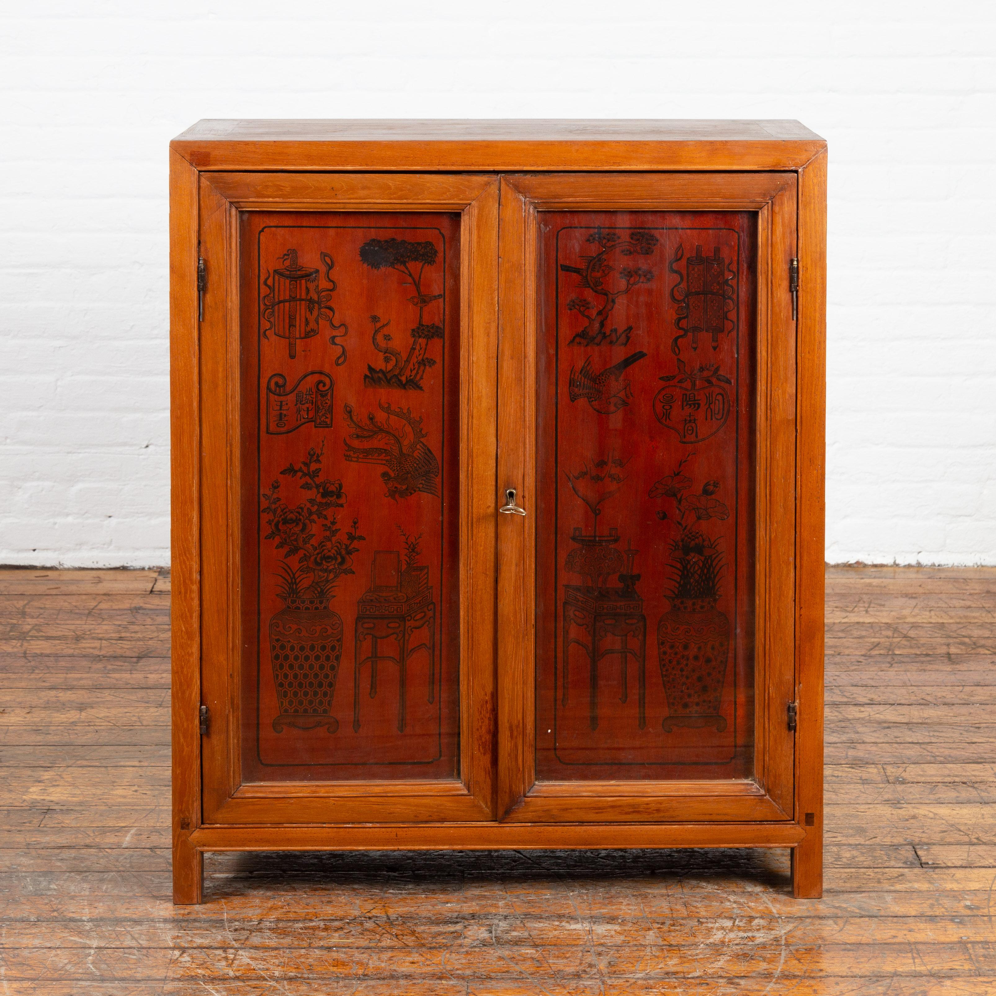 An antique Chinese cabinet from the early 20th century, with ink decorated panels behind glass doors. Created in China during the early years of the 20th century, this two-toned cabinet features a rectangular top sitting above two doors made of