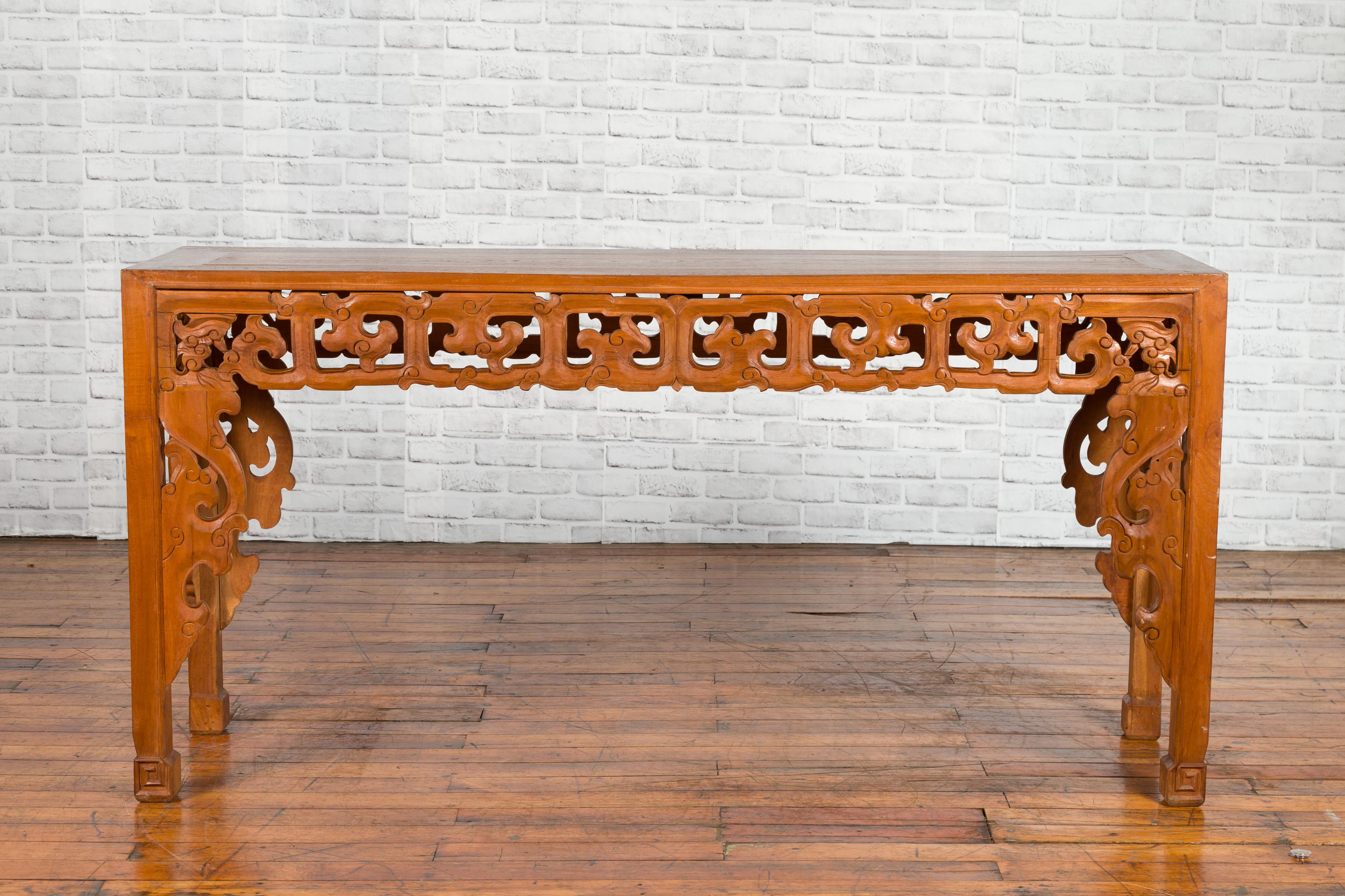 A Chinese altar console table from the early 20th century, with cloudy carved apron and scrolling feet. Created in China during the early years of the 20th, this wooden console table features a rectangular top with central board, sitting above a