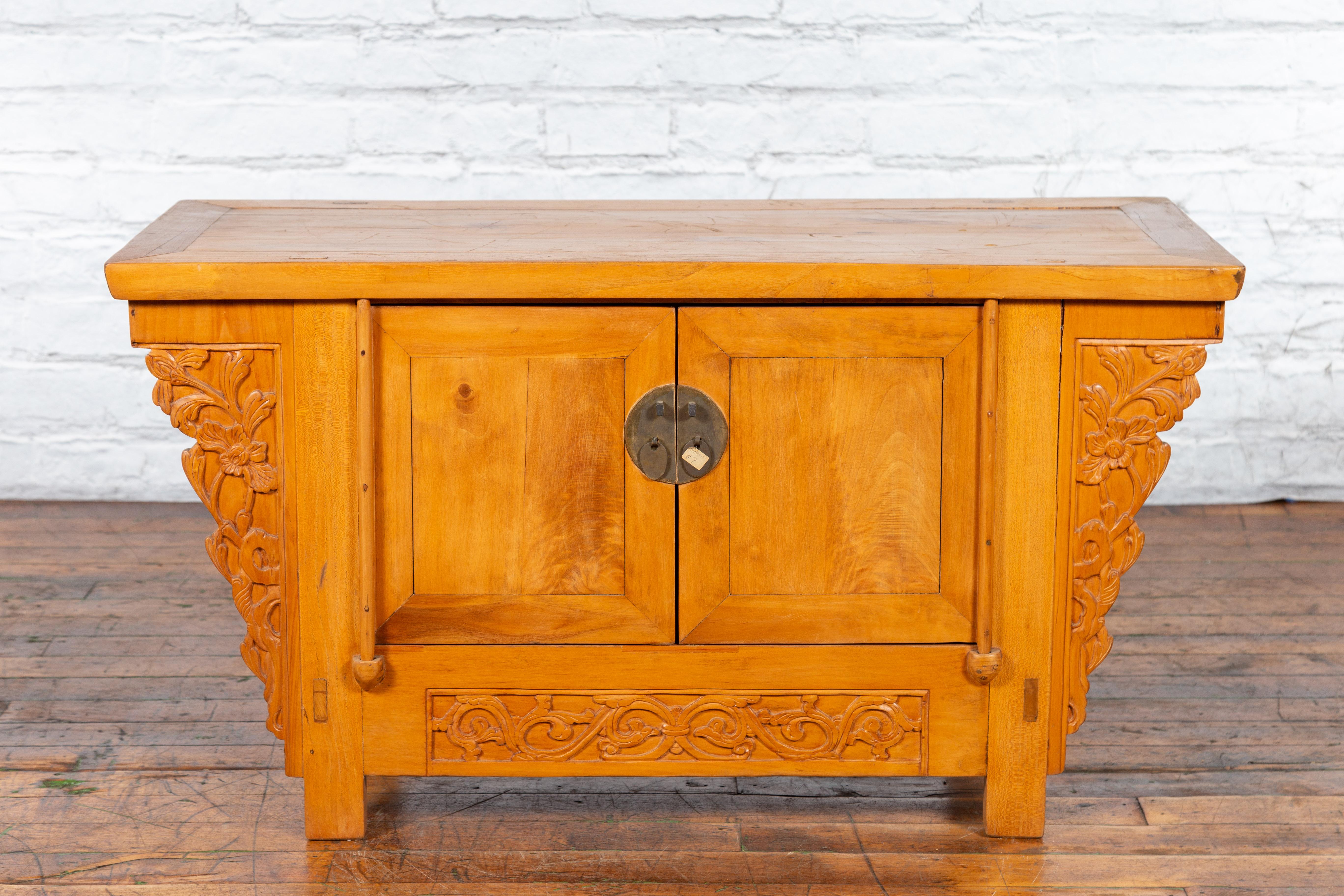 An antique Chinese elmwood sideboard from the early 20th century, with carved spandrels and bronze hardware. Created in China during the early years of the 20th century, this elm sideboard features a rectangular top with central board, sitting above