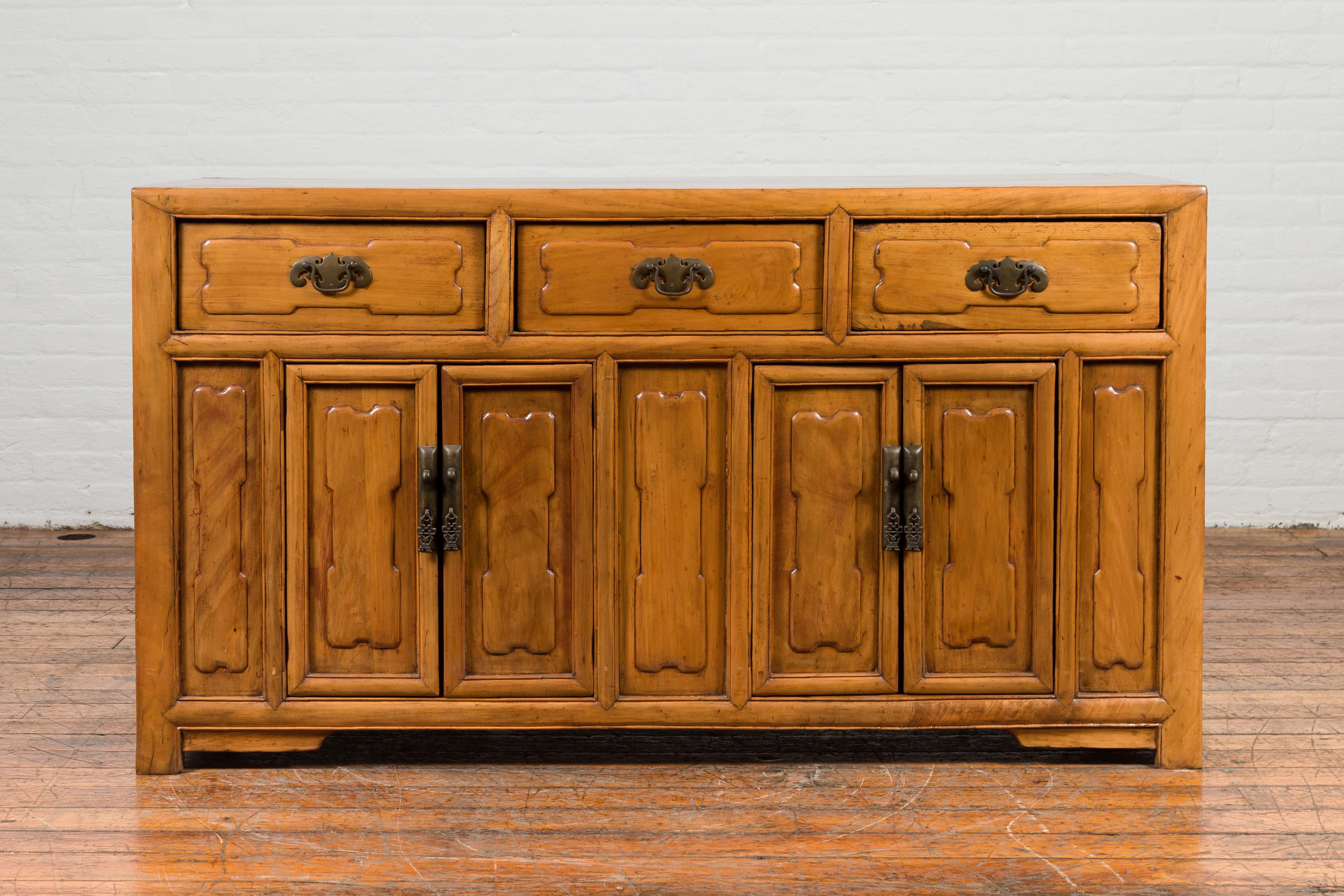 An antique Chinese elmwood sideboard from the early 20th century, with raised panels and three drawers over four doors. Created in China during the early years of the 20th century, this sideboard features a rectangular top with central board,