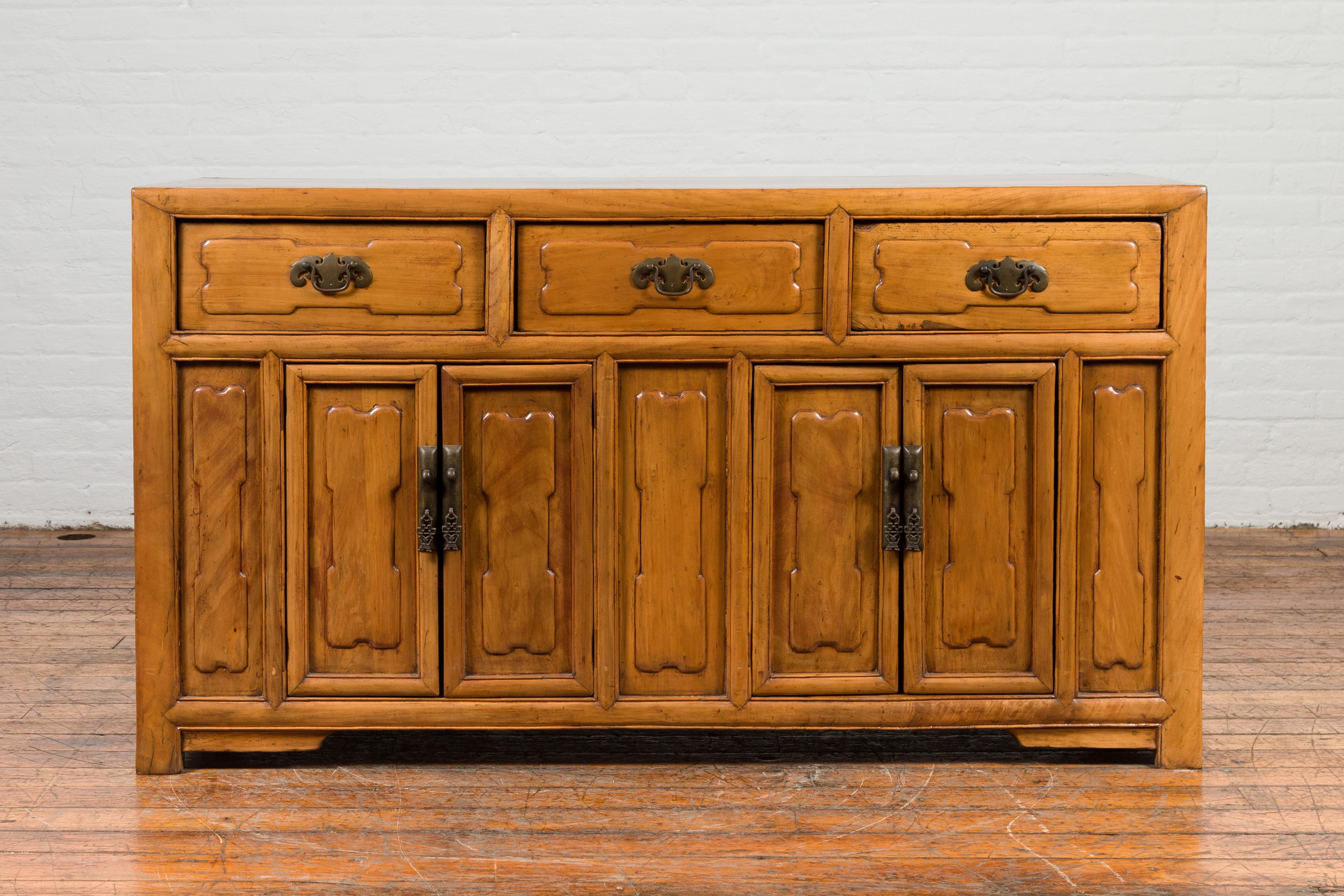 Antica credenza cinese in legno di olmo dei primi del Novecento, con pannelli in rilievo e tre cassetti su quattro ante. Creata in Cina nei primi anni del XX secolo, questa credenza presenta un piano rettangolare con tavola centrale, che si trova