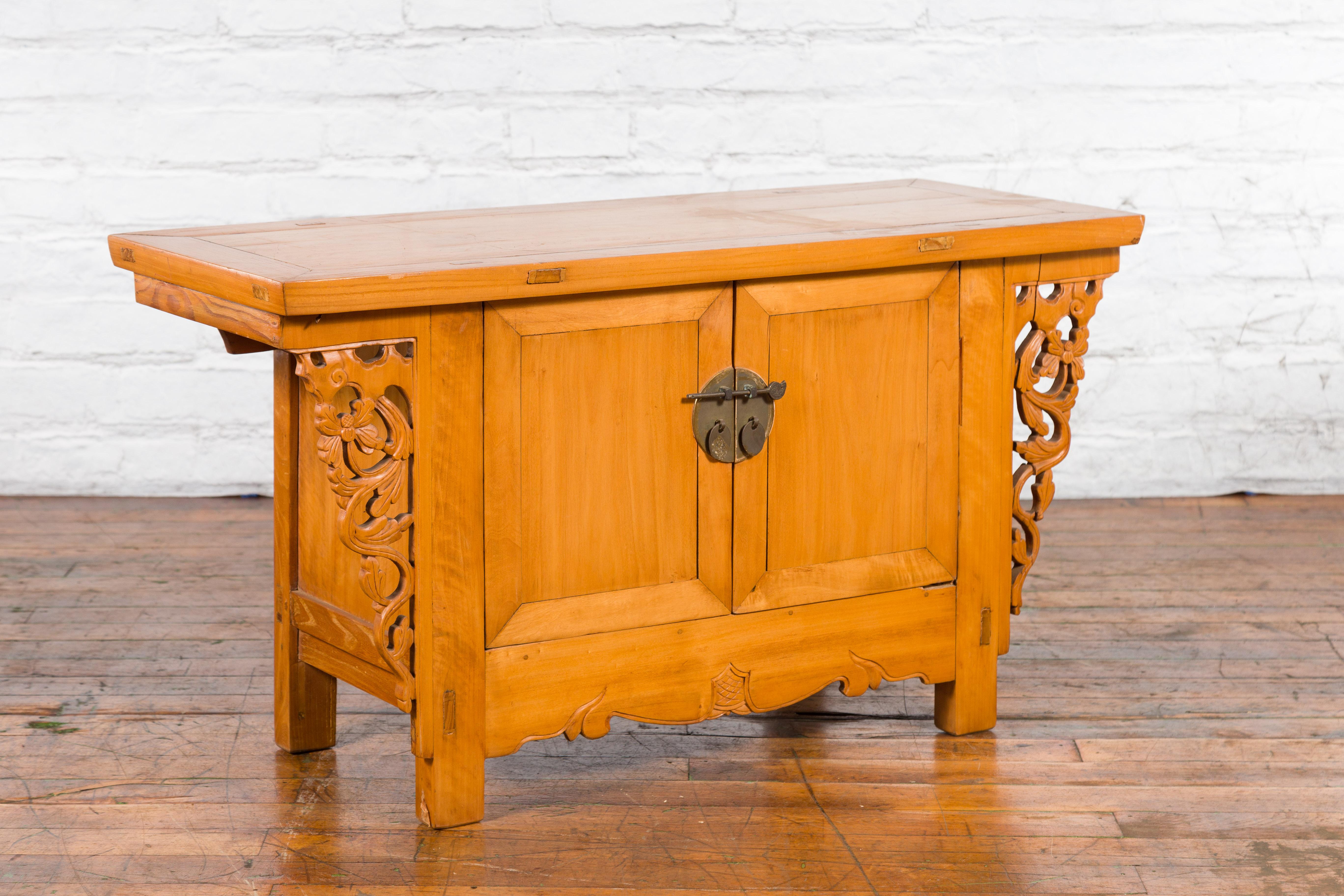 A small Chinese elmwood altar coffer sideboard from the early 20th century, with carved spandrels and brass hardware. Created in China during the early years of the 20th century, this elm coffer features a rectangular top with central board, sitting