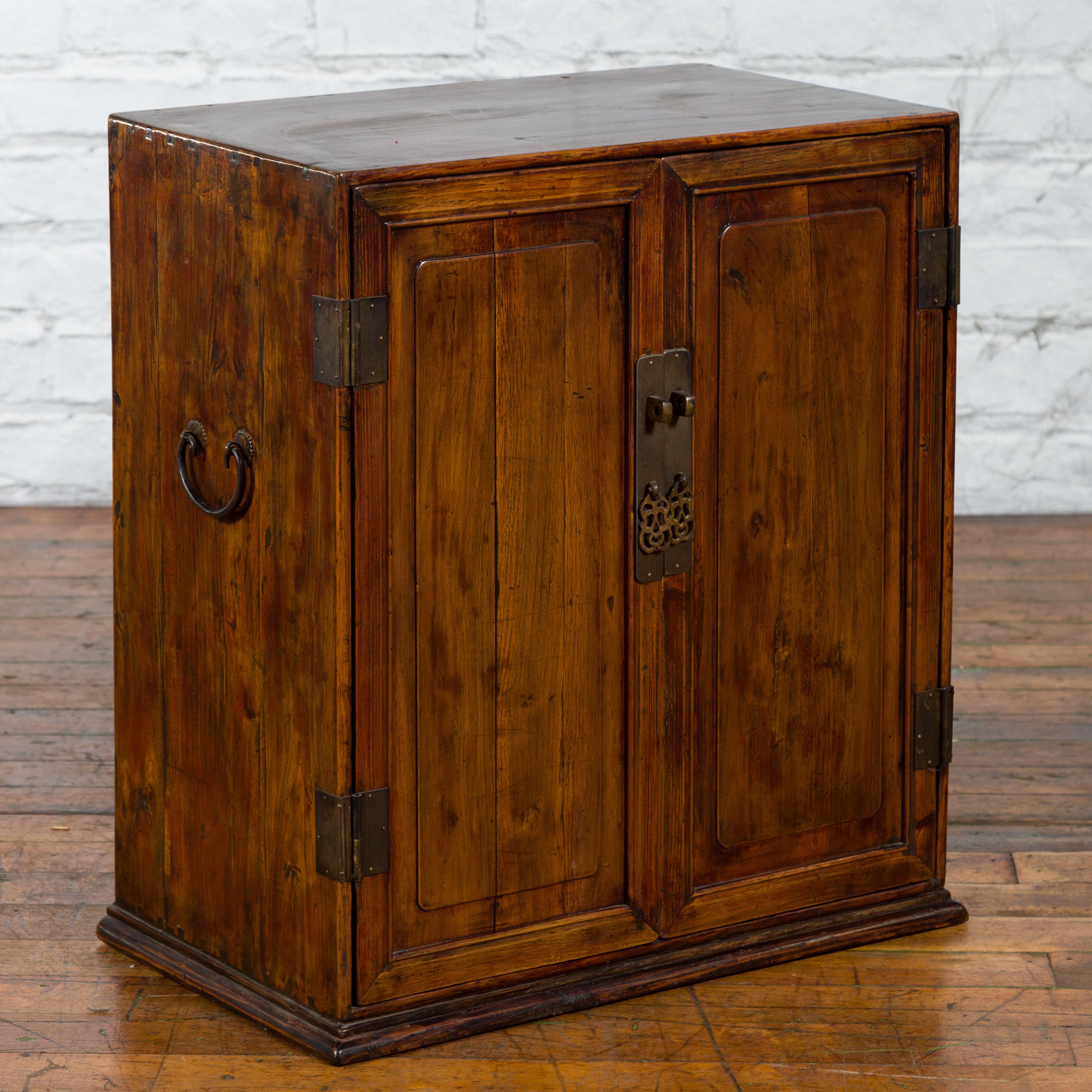 An antique Chinese elm wood side cabinet from the early 20th century, with slightly raised panels and brass hardware. Created in China during the early years of the 20th century, this low side cabinet features a linear silhouette perfectly