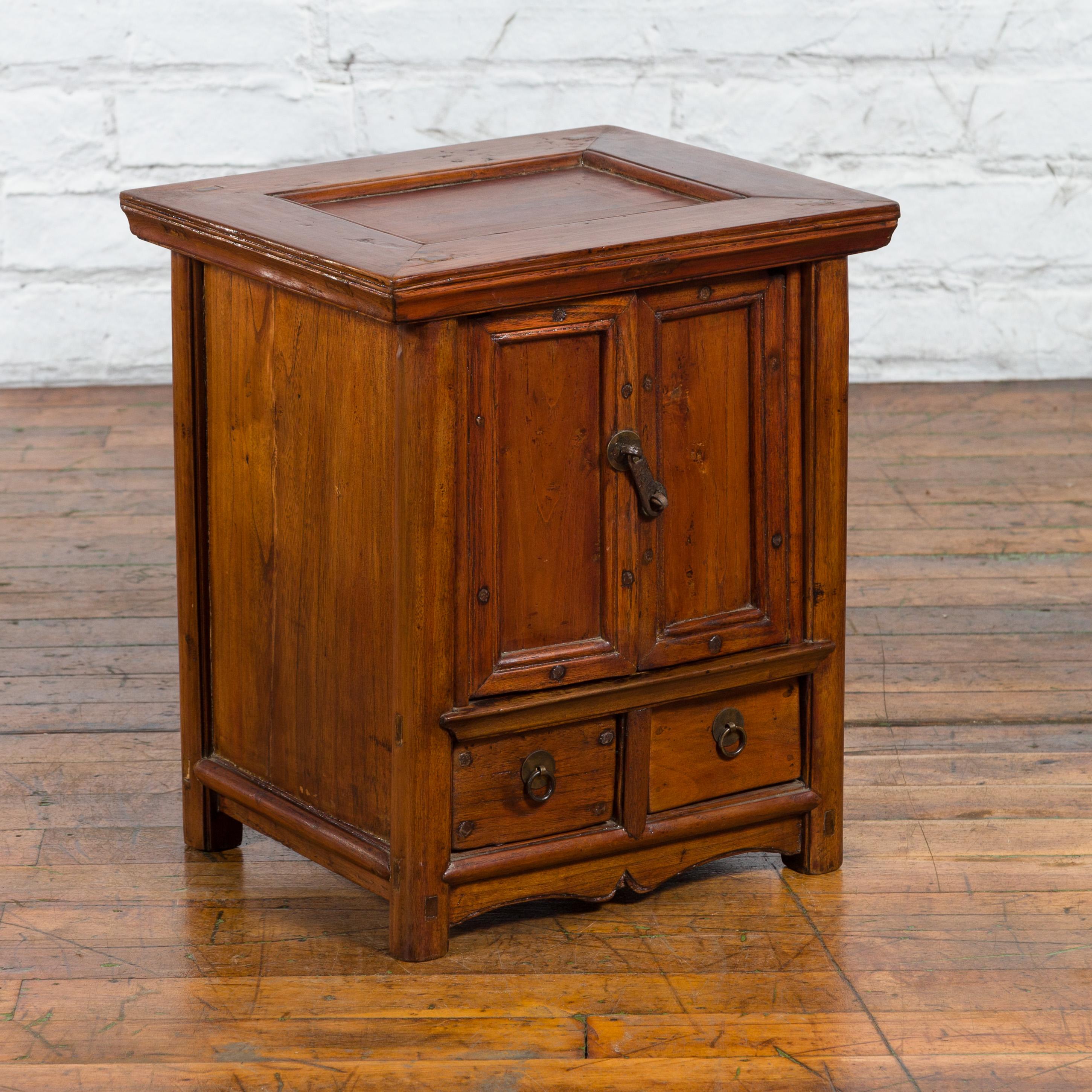 An antique Chinese elm wood bedside cabinet from the early 20th century with double doors, two drawers and brass hardware. Created in China during the early years of the 20th century, this elm wood bedside cabinet features a rectangular top with