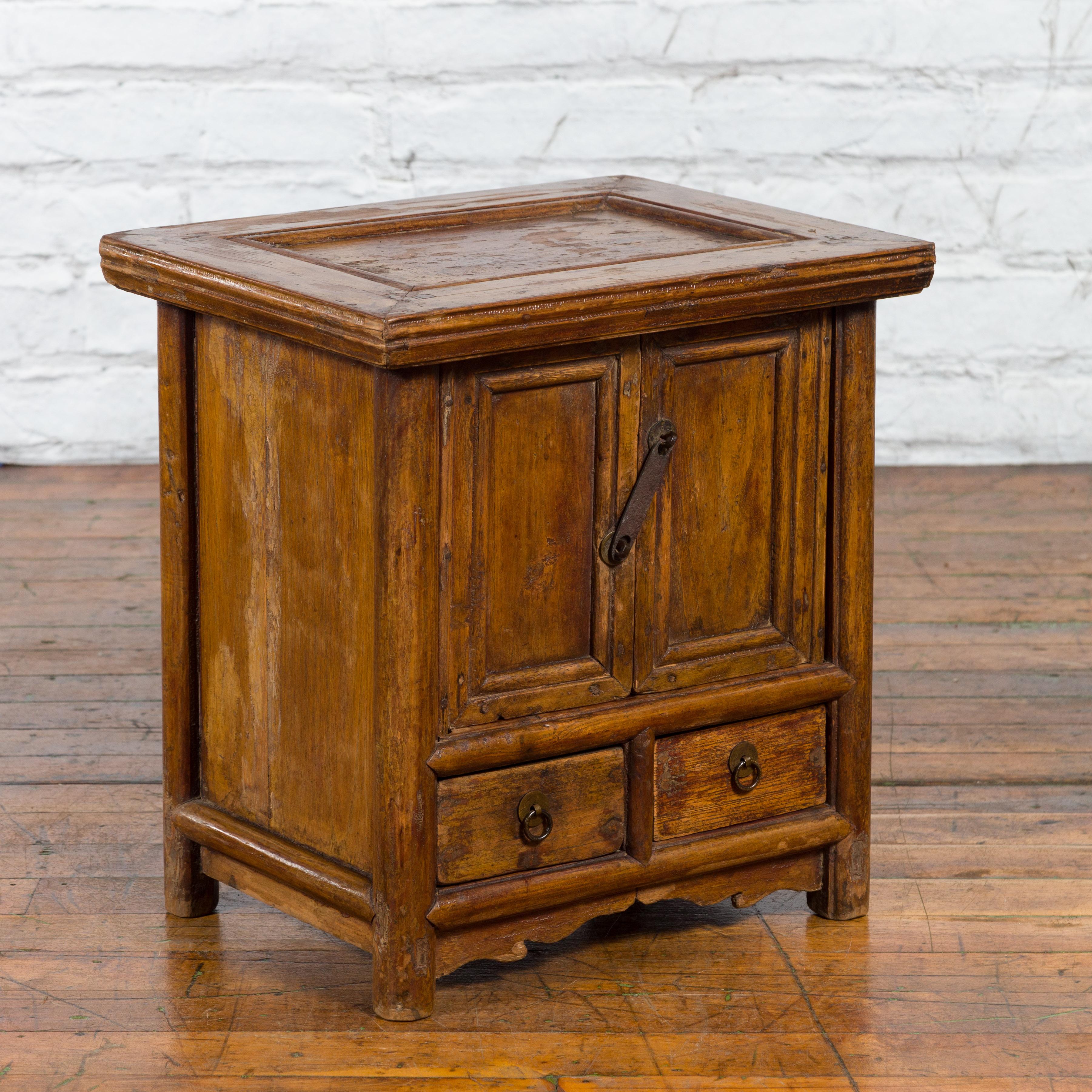 A Chinese antique elm wood bedside cabinet from the early 20th century, with double doors, two drawers, iron hardware and weathered patina. Created in China during the early years of the 20th century, this elm wood bedside cabinet features a