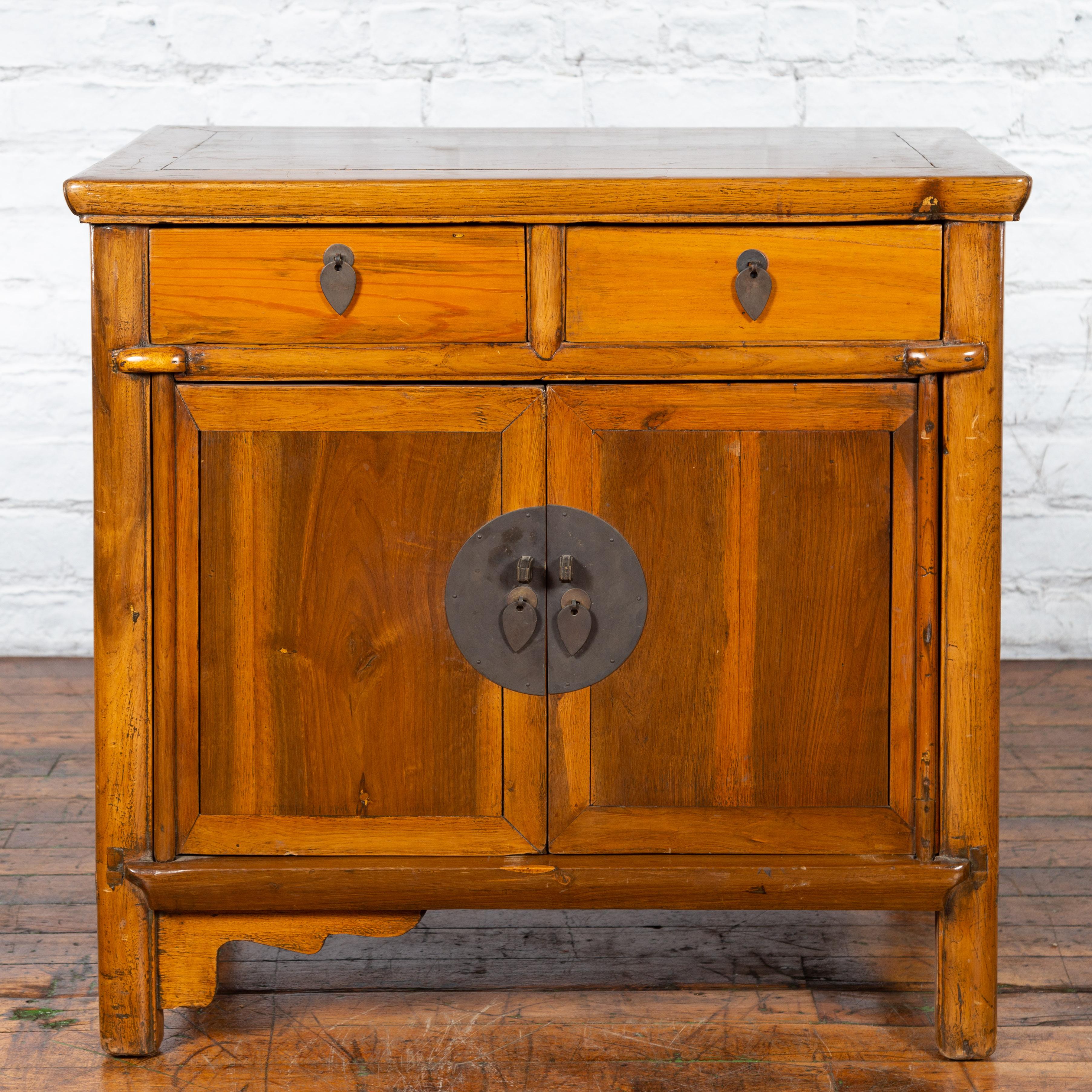 A Chinese elmwood side chest from the early 20th century, with round bronze medallion hardware, two drawers over two doors. Created in China during the early years of the 20th century, this elmwood side chest features a rectangular top with central