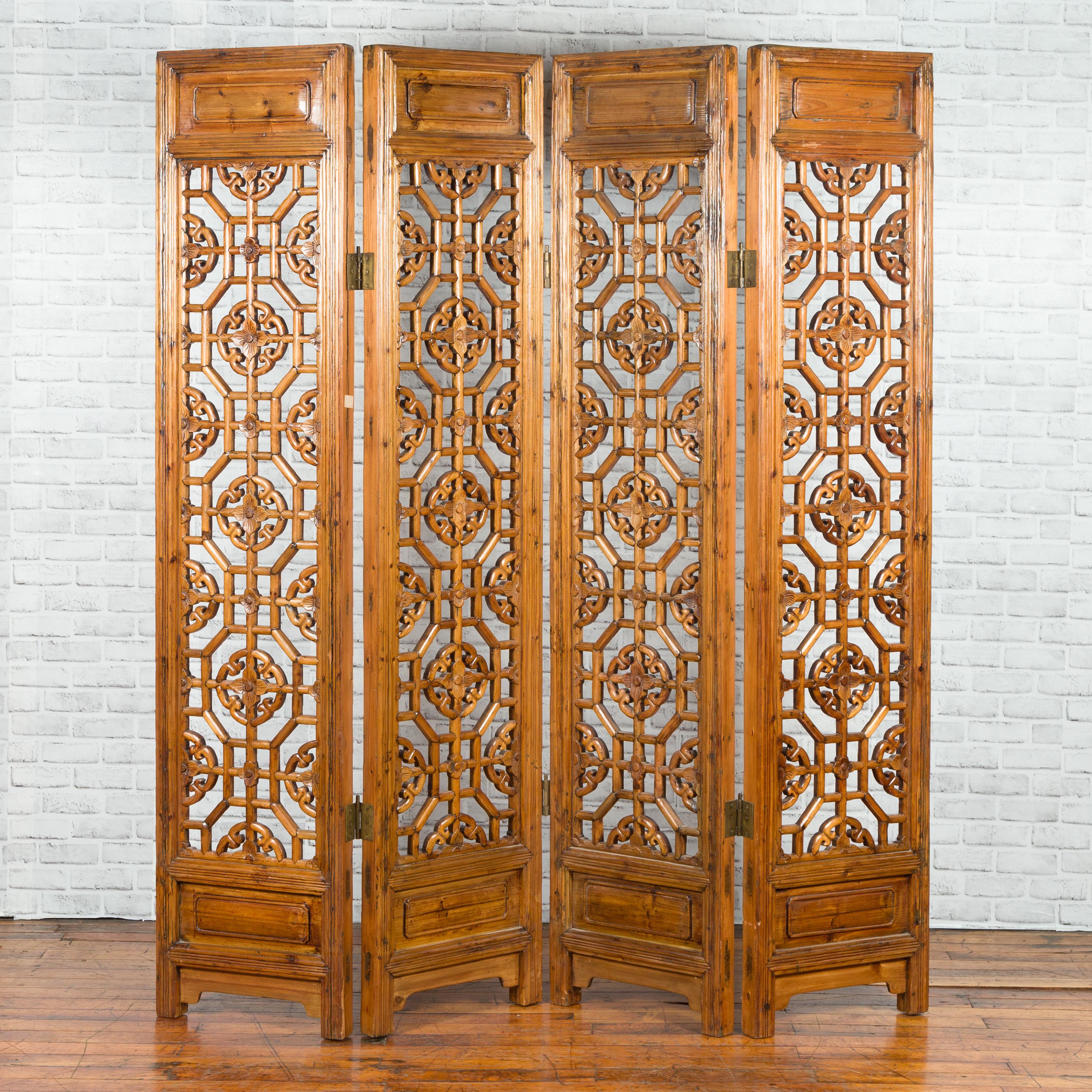 A Chinese fretwork four-panel screen from the early 20th century, with geometric motifs and floral accents. Created in China during the early years of the 20th century, this wooden screens features four vertical fretworks panels adorned with