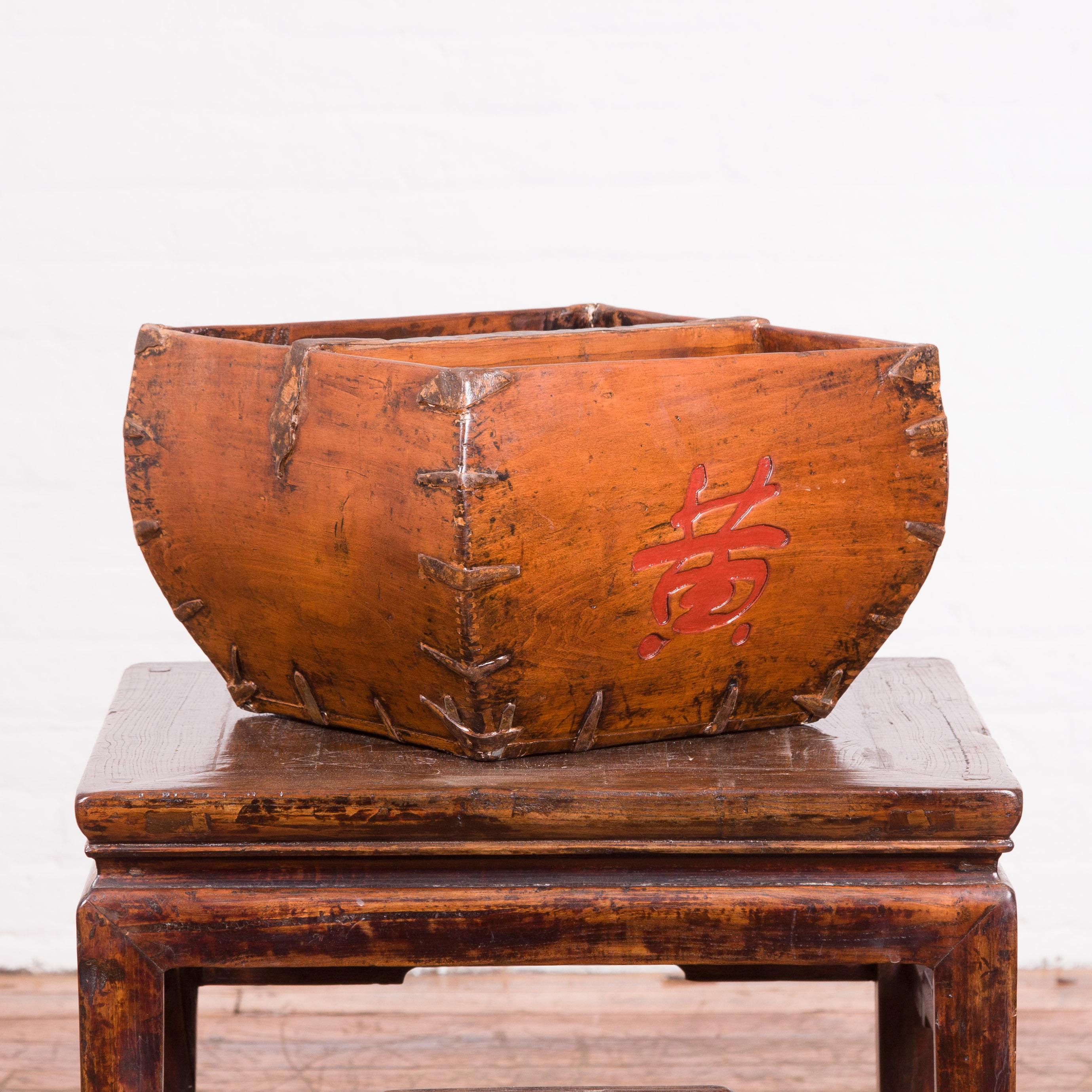 A Chinese antique grain basket from the early 20th century, with red calligraphy. Created in China during the early years of the 20th century, this grain basket features a square tapering body accented with braces in the corners and red calligraphy