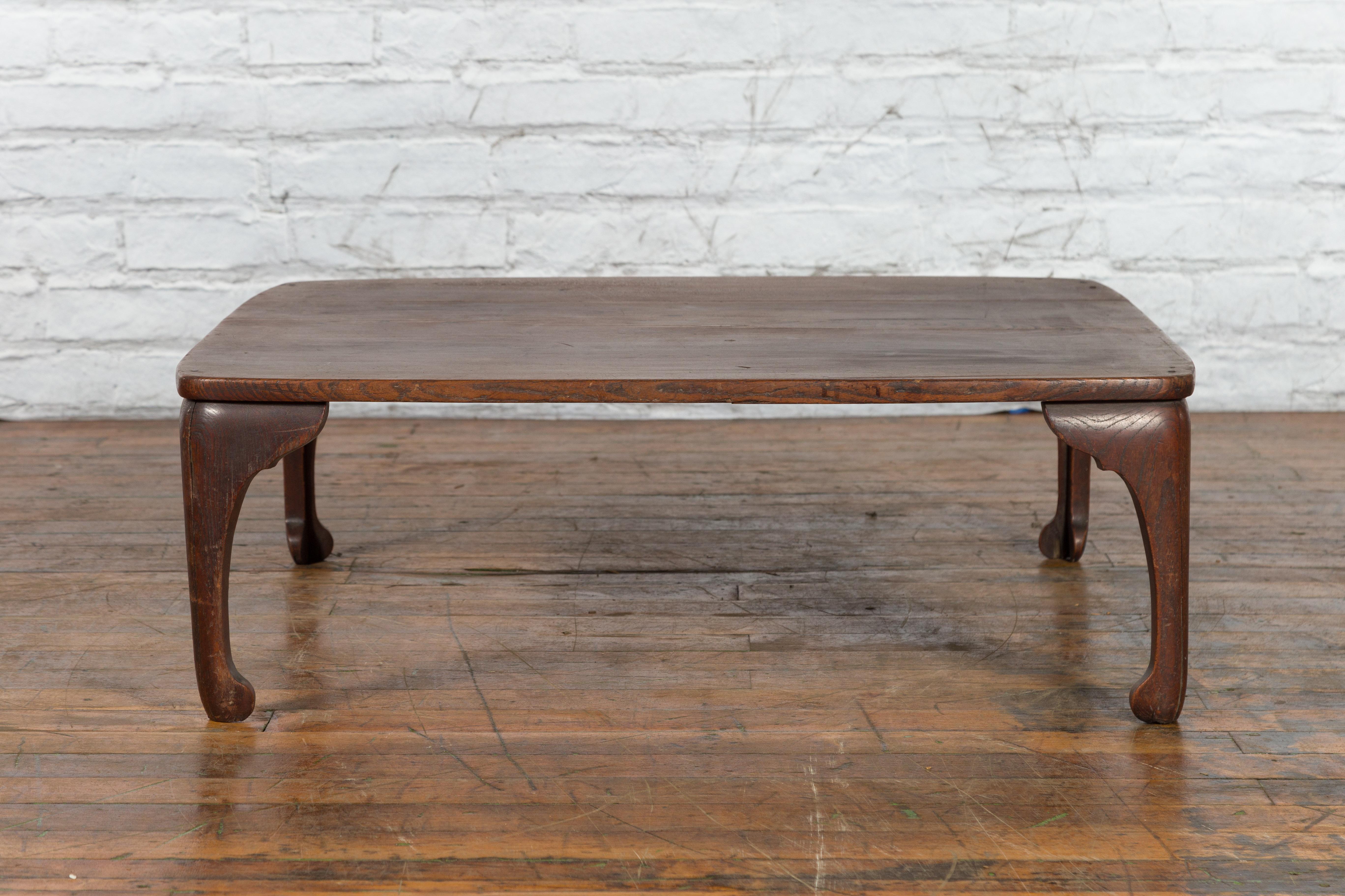 A Chinese antique low wooden table from the early 20th century, with curving legs. Created in China during the early years of the 20th century, this low wooden table features a simple rectangular top sitting above four delicately curving legs.