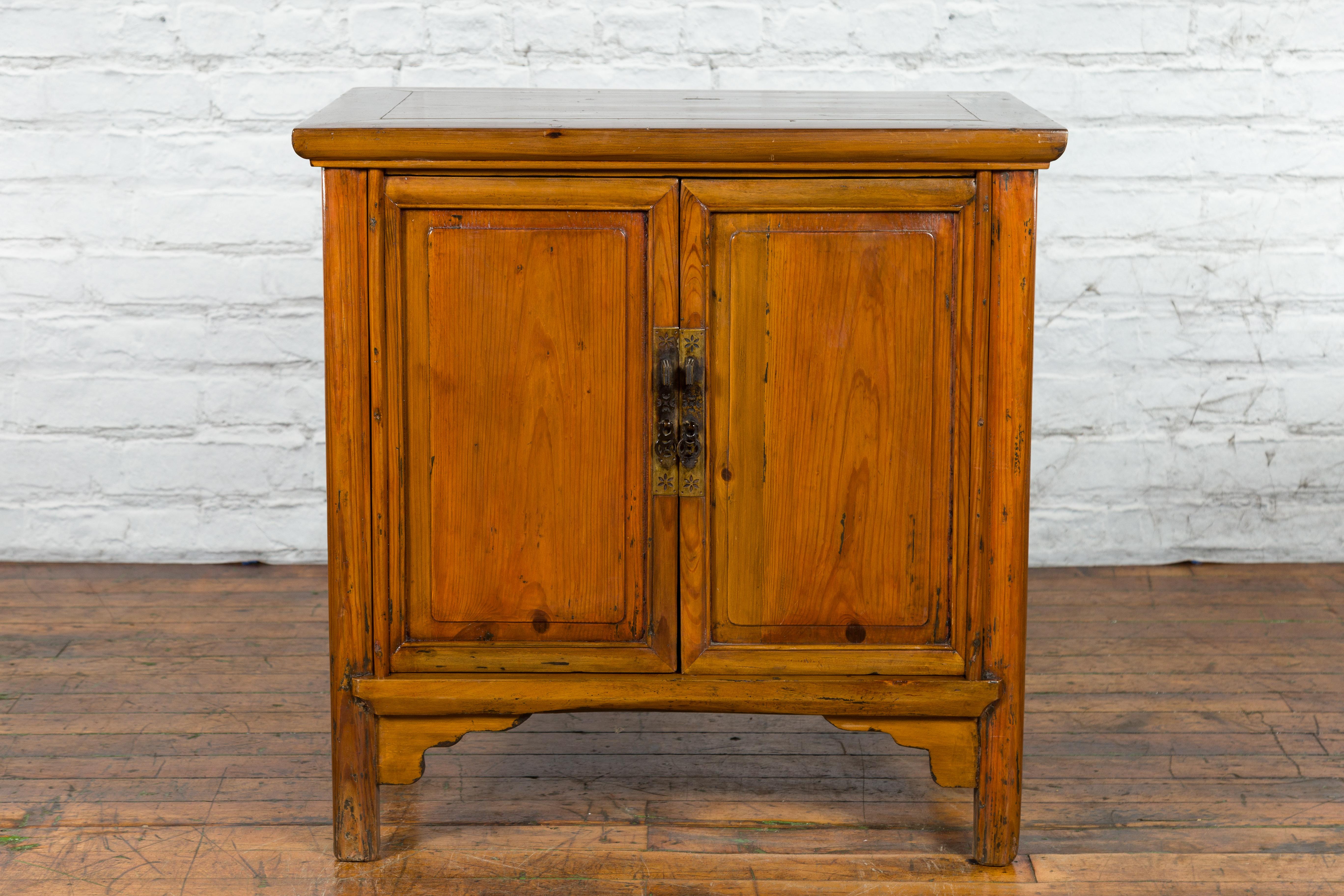A Chinese natural lacquer side cabinet from the early 20th century, with brass hardware. Created in China during the early years of the 20th century, this side cabinet features a rectangular top with central board, sitting above two doors fitted