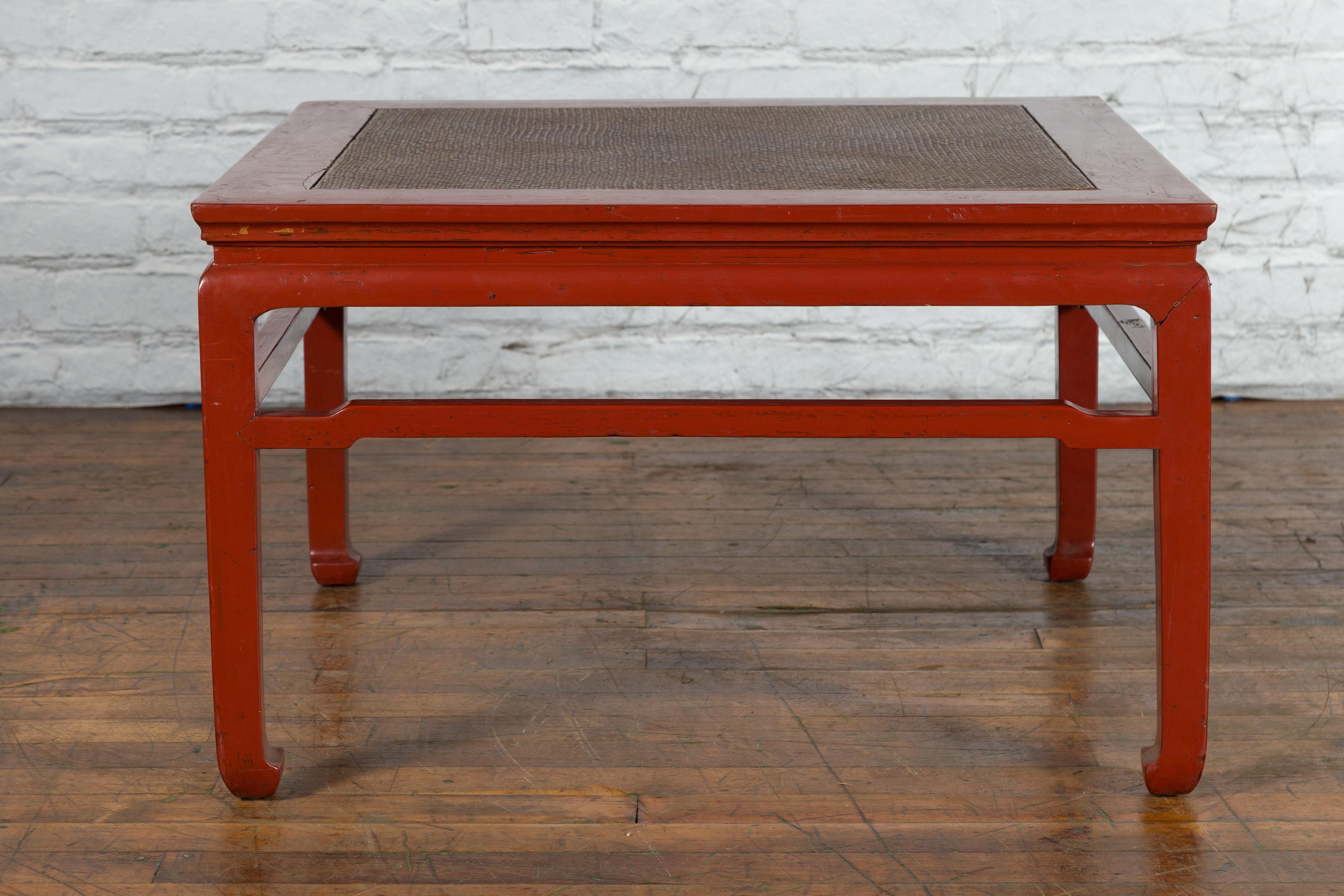 An antique Chinese wooden coffee table from the early 20th century, with red lacquer ground, hand woven rattan top, humpback stretcher on all sides and horse hoof legs. Created in China during the early years of the 20th century, this antique coffee