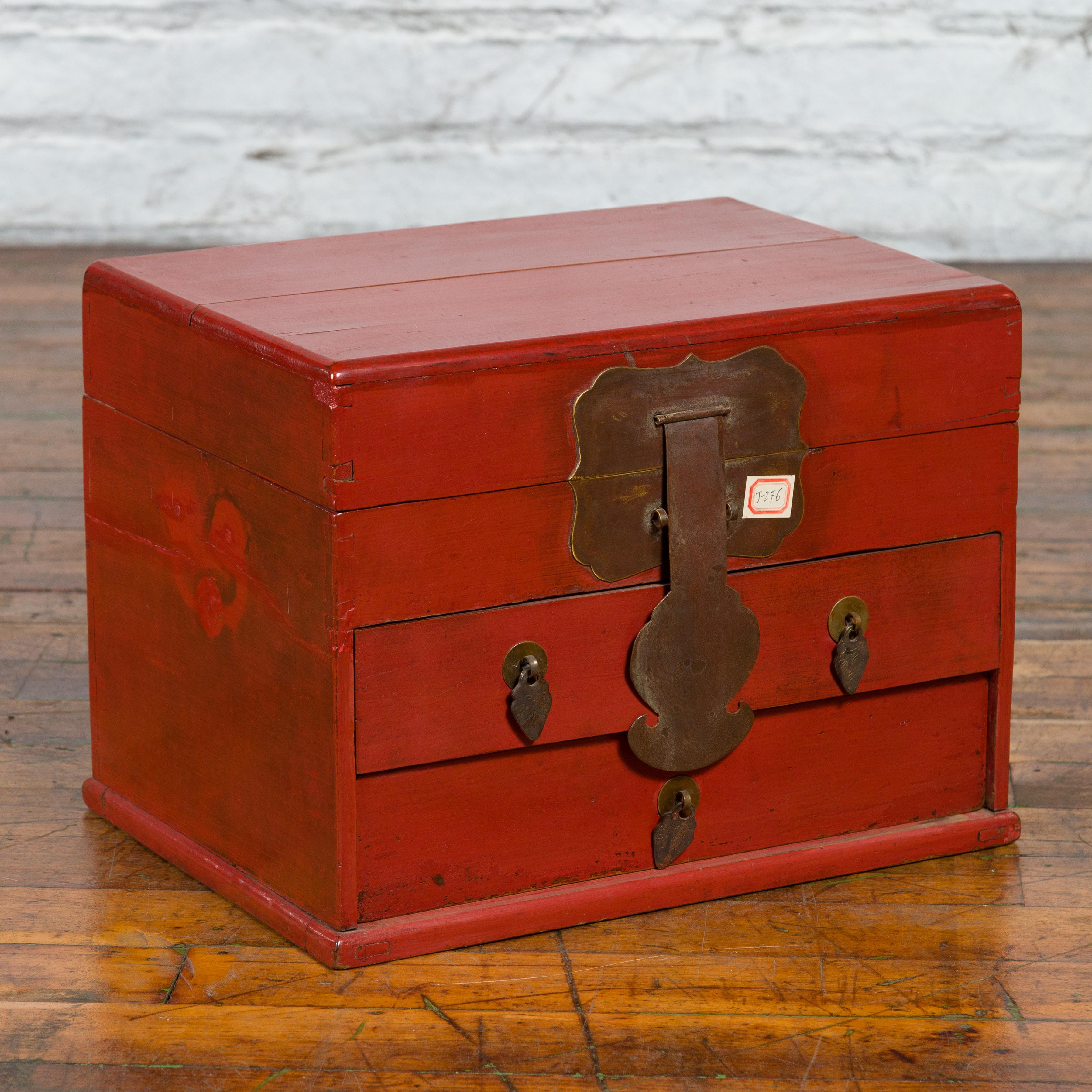 A Chinese red lacquered jewelry box from the early 20th century, with lidded top and three drawers. Created in China during the early years of the 20th century, this jewelry box attracts our attention with its red lacquer and large bronze hardware.