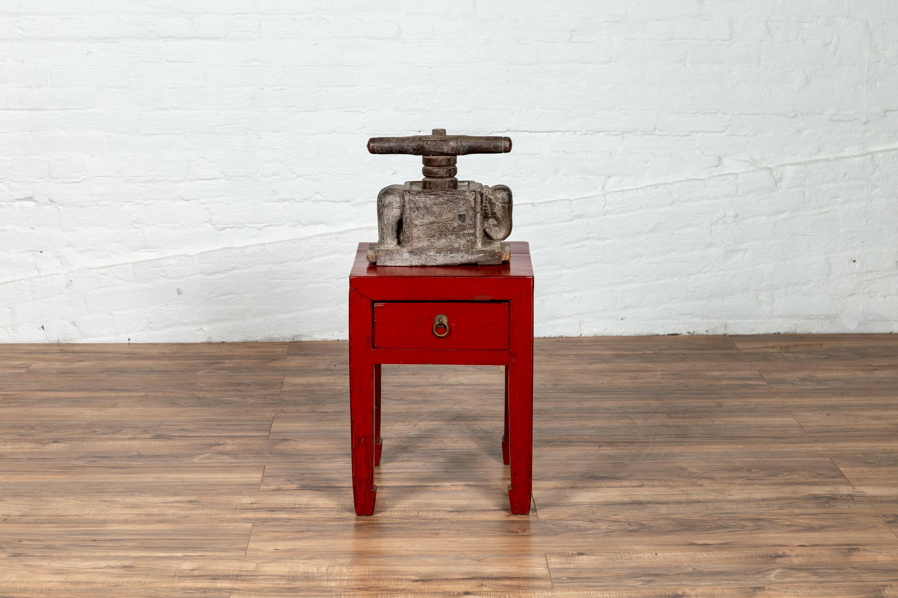 A Chinese red lacquered stool from the early 20th century, with single drawer and horse-hoof legs. This lovely Chinese stool features a square top sitting above a single drawer fitted with a brass ring pull adorned with a flower-shaped backplate,