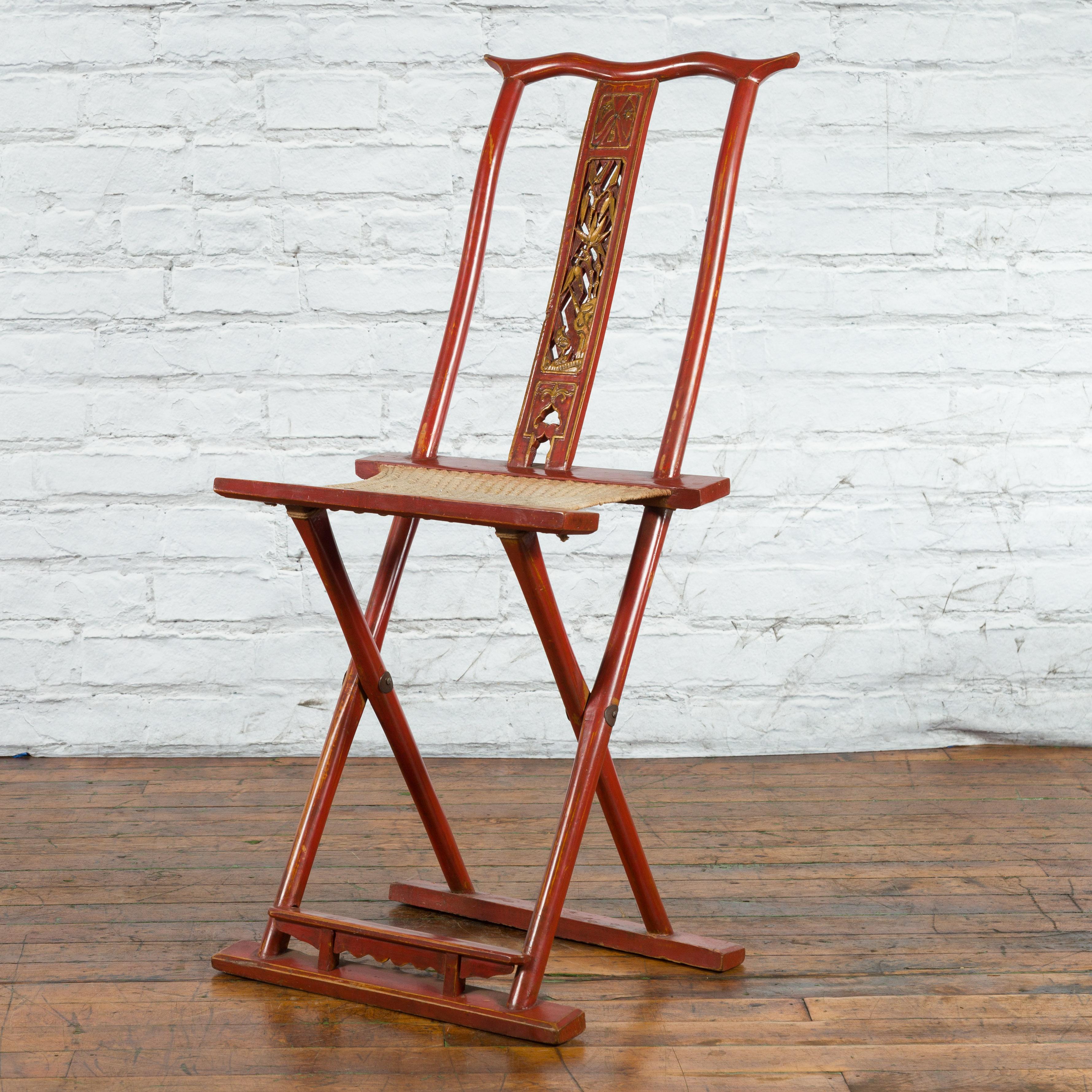 Ancienne chaise de voyage pliante chinoise laquée rouge du début du XXe siècle, avec des motifs sculptés, un repose-pieds et un tissu tissé. Créée en Chine au cours des premières années du XXe siècle, cette chaise pliante présente un corps laqué