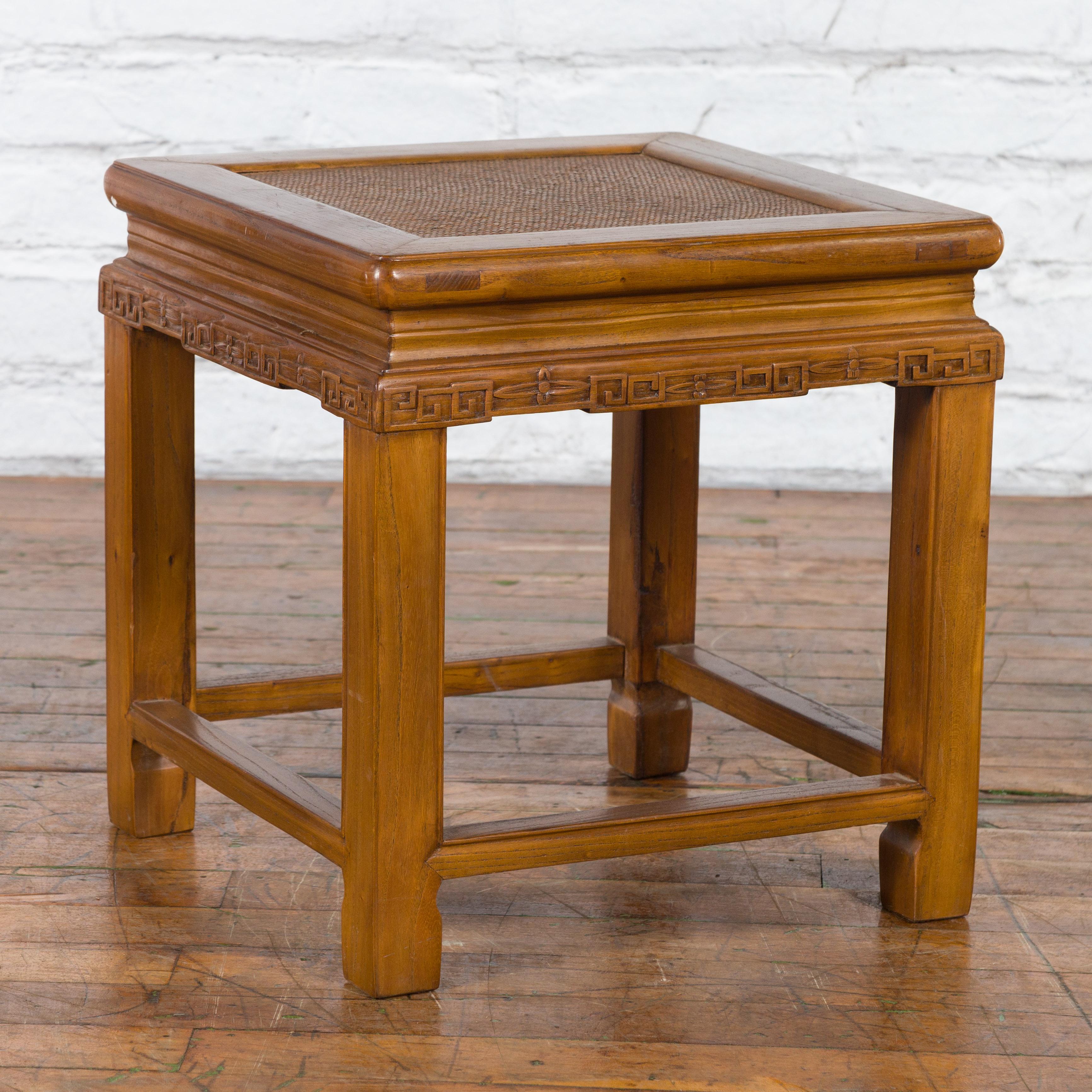 A Chinese antique side table from the early 20th century with carved apron, hand-woven rattan top and low stretchers. Created in China during the early years of the 20th century, this side table features a square top with woven rattan inset, sitting