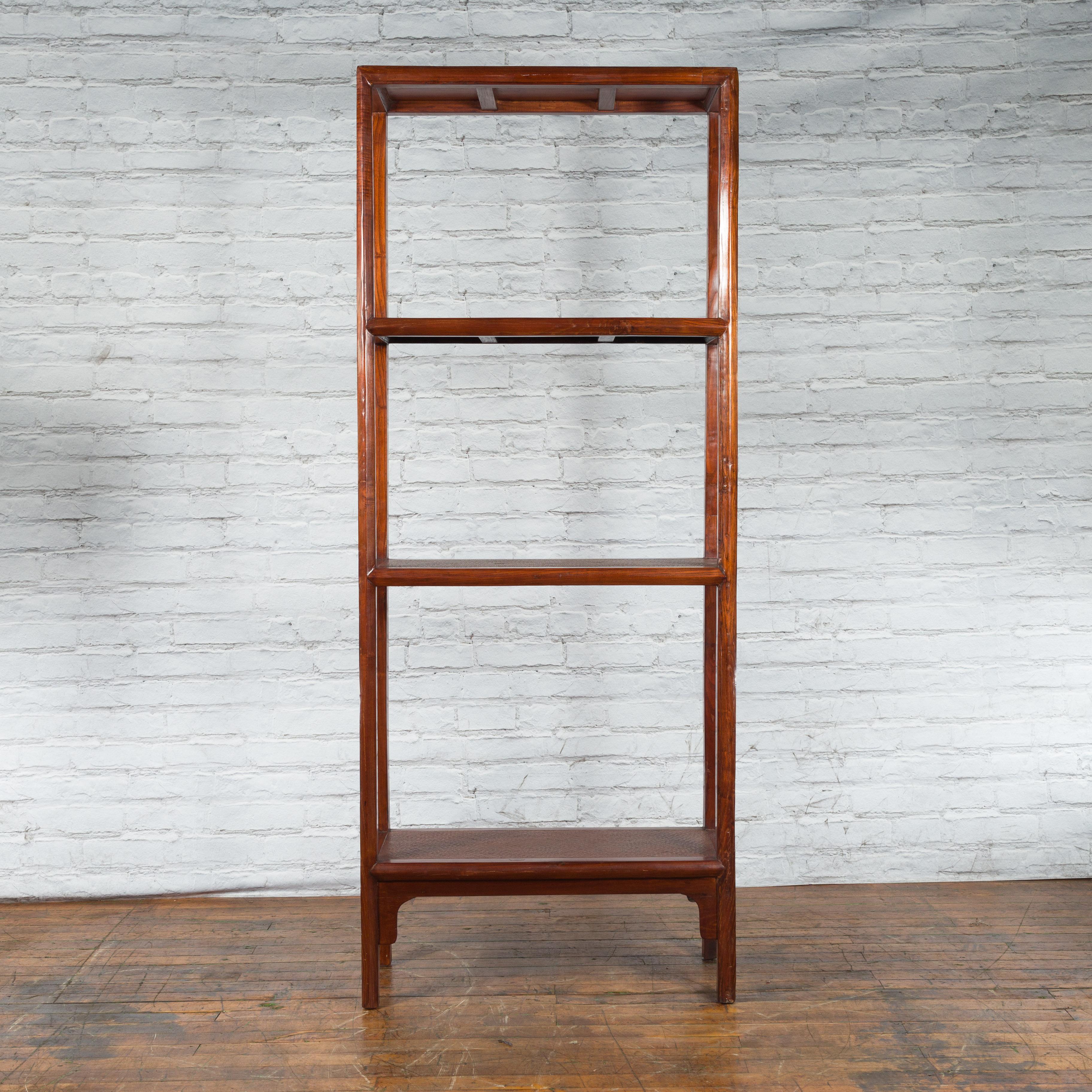 A Chinese elm wood bookshelf from the early 20th century with rattan shelves and carved apron. Created in China during the early years of the 20th century, this elm wood bookshelf features an open structure made of three shelves presenting woven