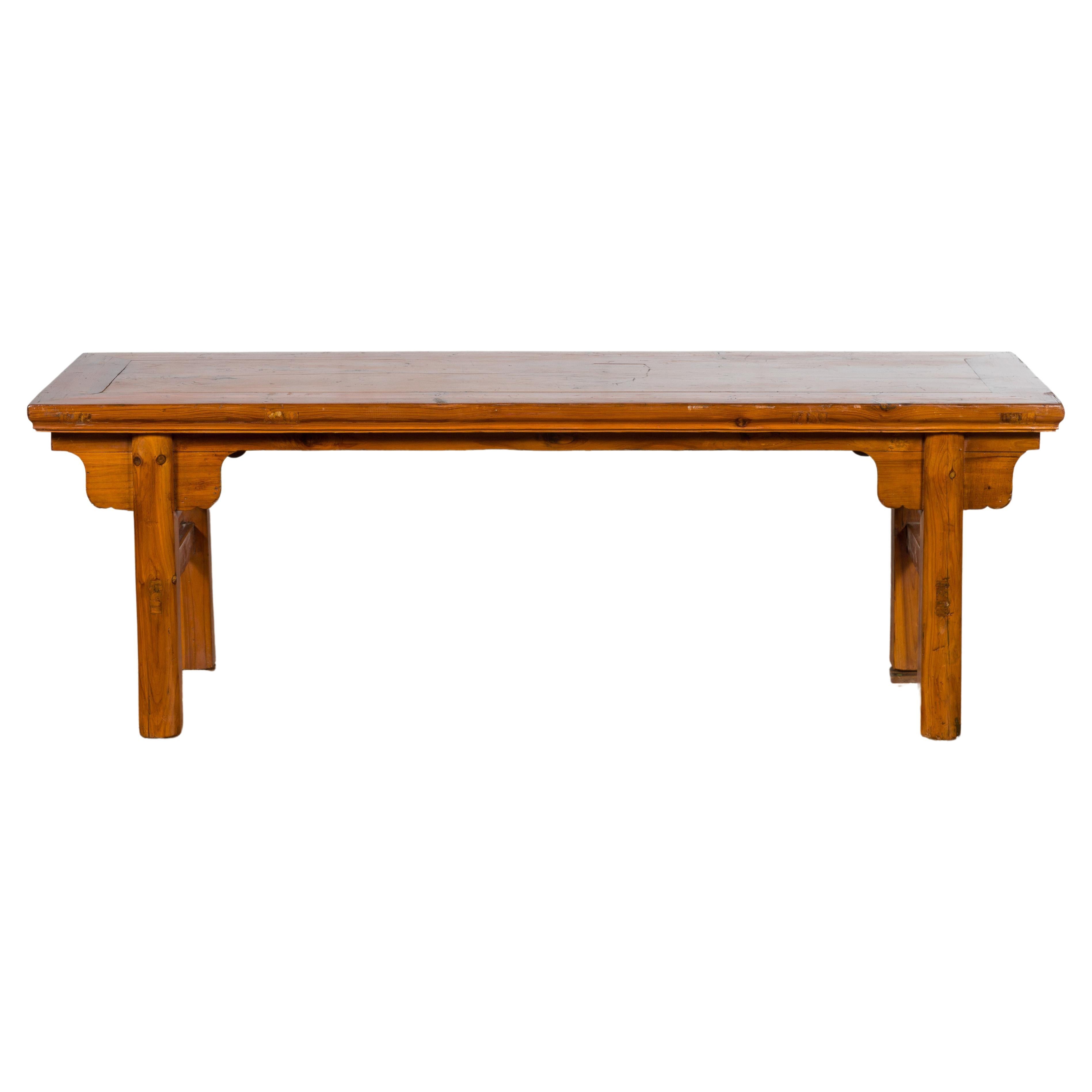 An antique Chinese cocktail table from the early 20th century, with carved spandrels and straight legs. Created in China during the early years of the 20th century, this cocktail table features a rectangular top with central board, sitting above a