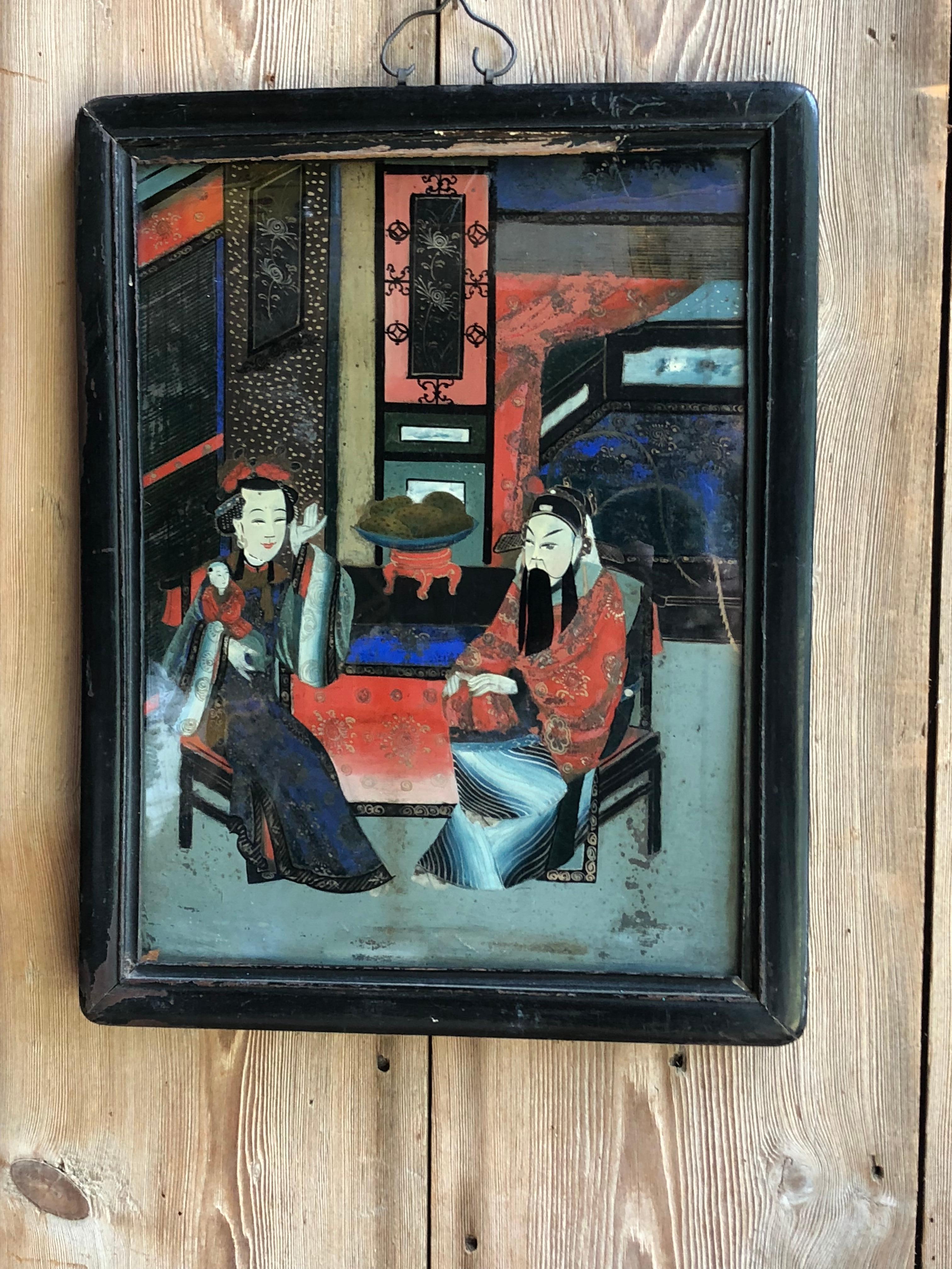 An early 19th century Chinese reverse painting on glass of a couple with a small child in a room, in original teak frame.