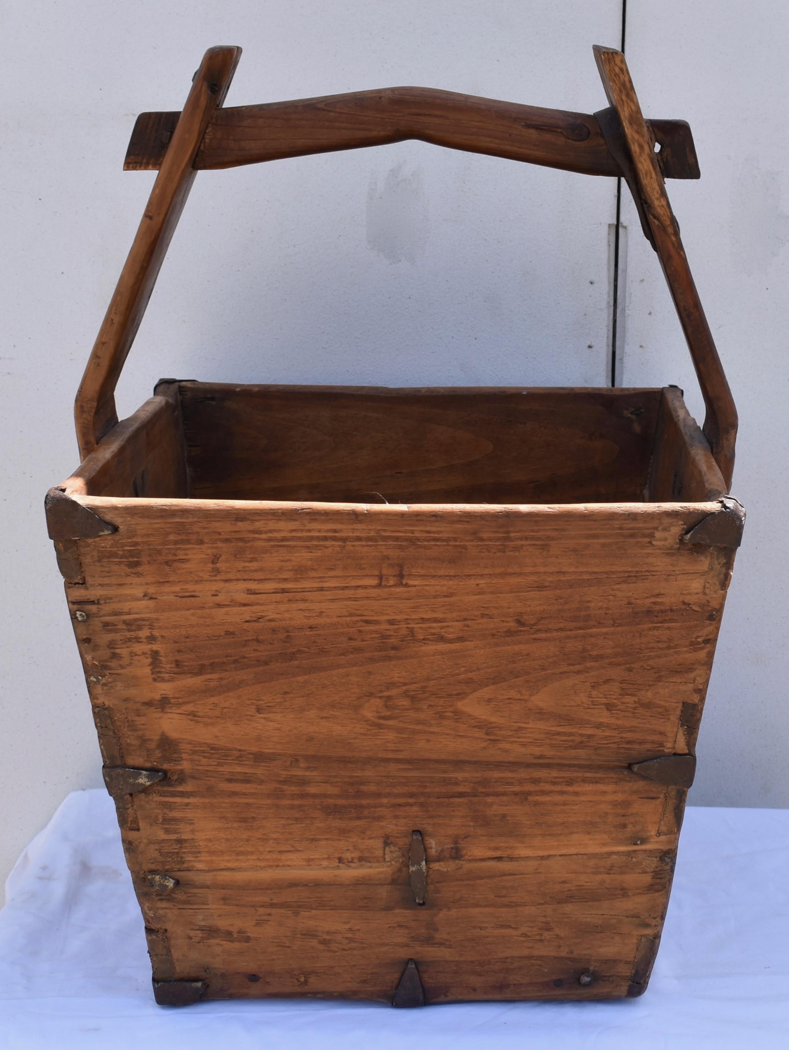 This is an outstanding Chinese dovetailed Elm bucket, used for carrying and measuring rice. The wedge-shaped slatted box has hammered iron reinforcements on the top corners and halfway down each side. They were originally present, on all four bottom