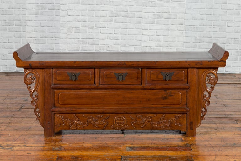 A Chinese Qing dynasty period elm kang cabinet with everted flanges, three drawers, carved spandrels and dragon motifs. Created in China during the Qing dynasty, this Chinese kang cabinet features a rectangular top with central board, flanked with