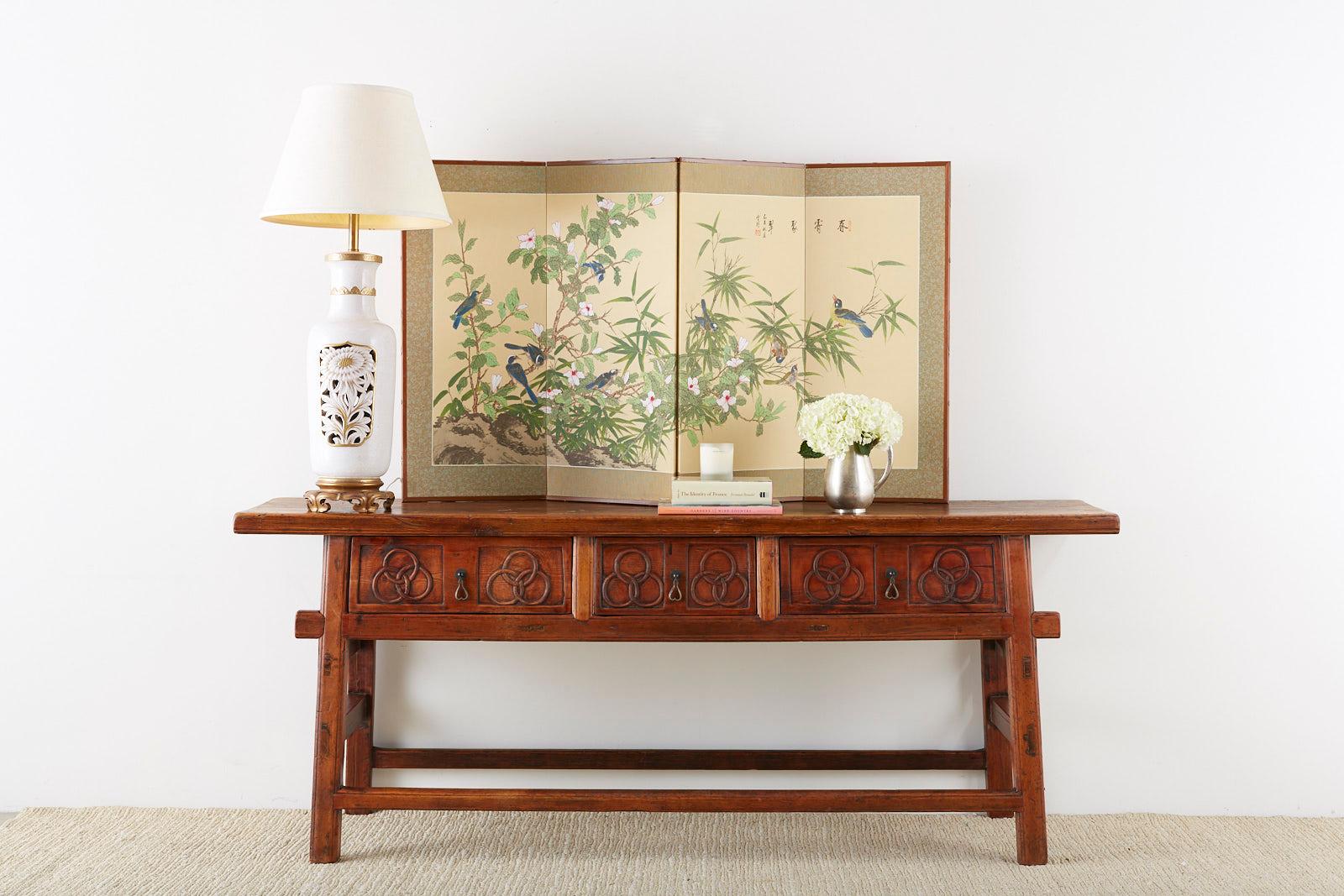 Magnificent Chinese trestle style altar table or console table constructed from hand carved elm. Featuring a thick rustic plank top over 2 inches thick. The table is fronted by three large storage drawers decorated with a three ring motif of