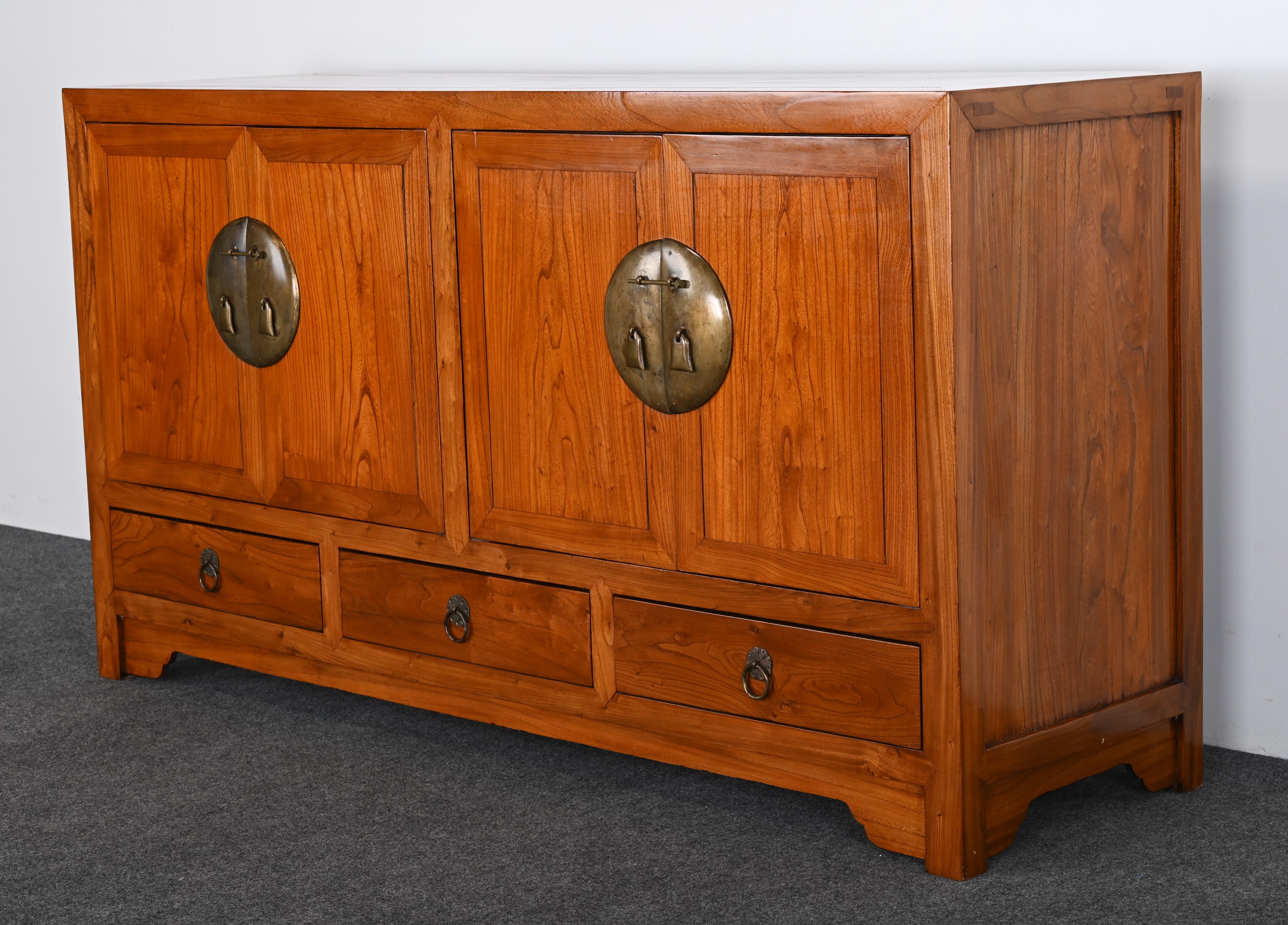 A handsome Chinese credenza or cabinet made of elmwood with brass hardware. This Asian sideboard has beautiful amber tones with mortise and tenon joints. The cabinet is functional with ample storage with open shelving and additional drawers. This