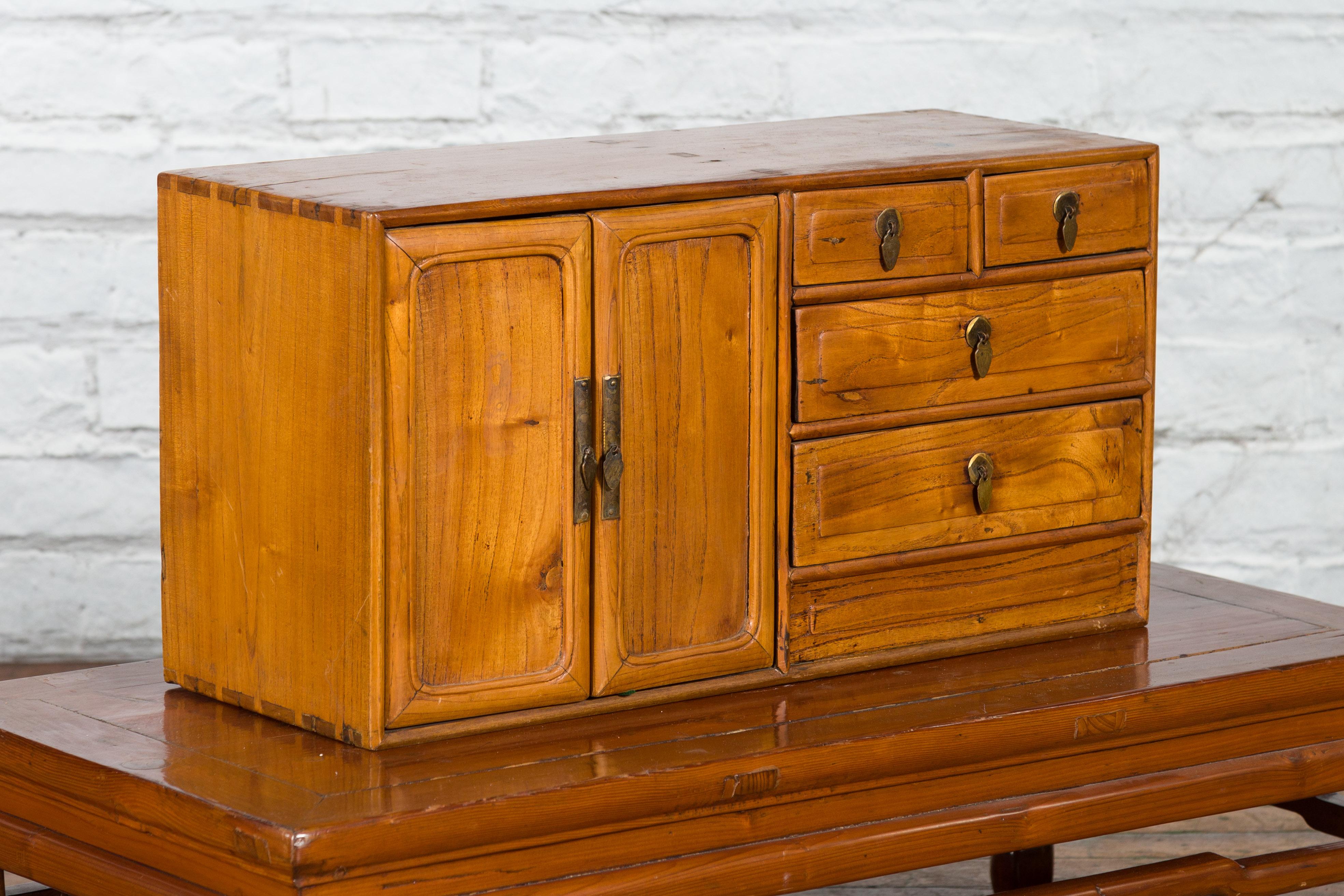 A Chinese elmwood makeup or jewelry chest from the early 20th century with five drawers and brass hardware. Created in China during the early years of the 20th century, this small elm wood makeup chest features a rectangular top with mortise and