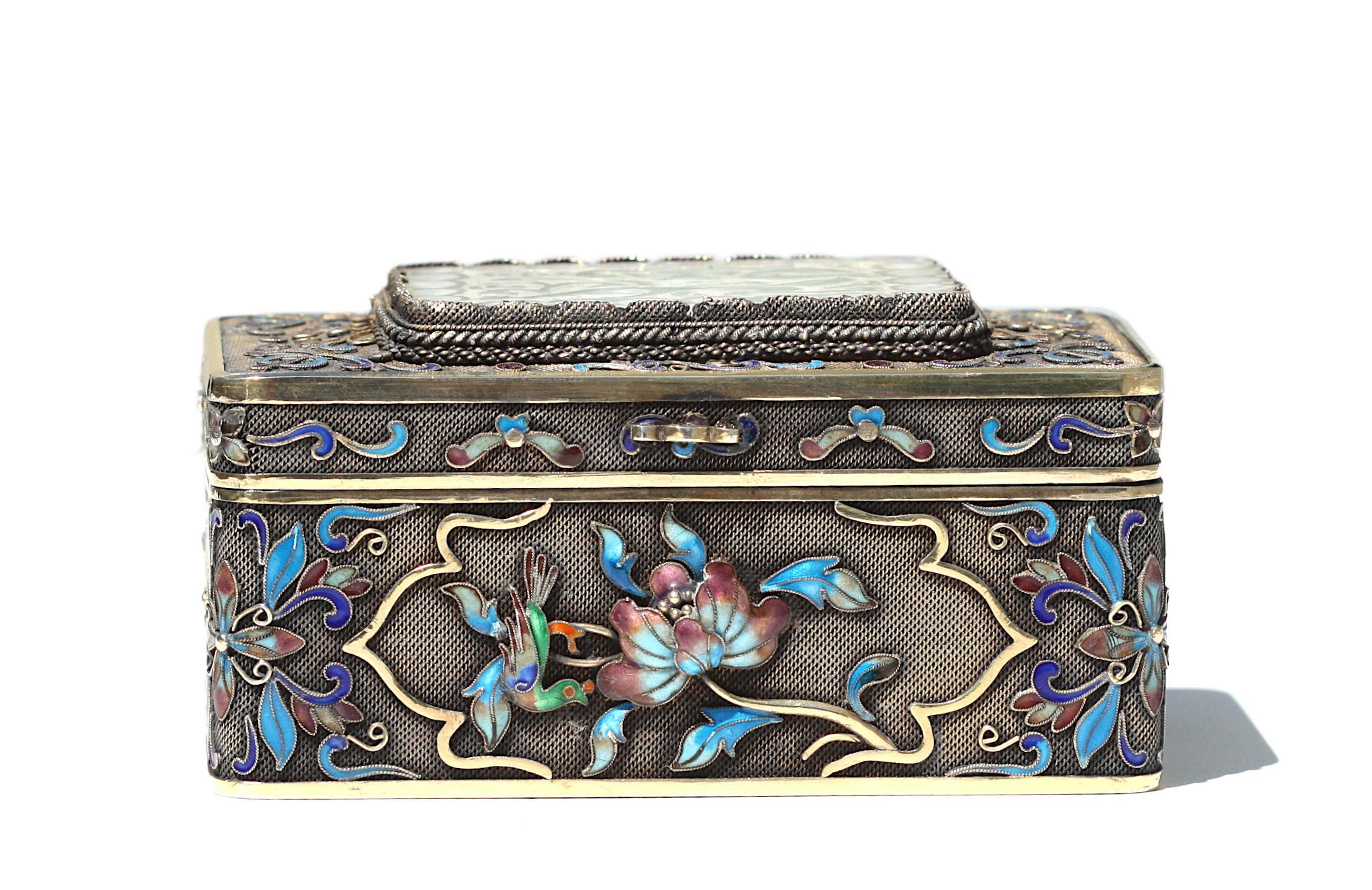 
Chinese Enamel and White Jade Mounted Silver Box
Late 19th/early 20th Century. The underside marked silver. The rectangular silver box with a hinged lid set with a jade panel pierced with a scrolling dragon, the top, and sides decorated with raised