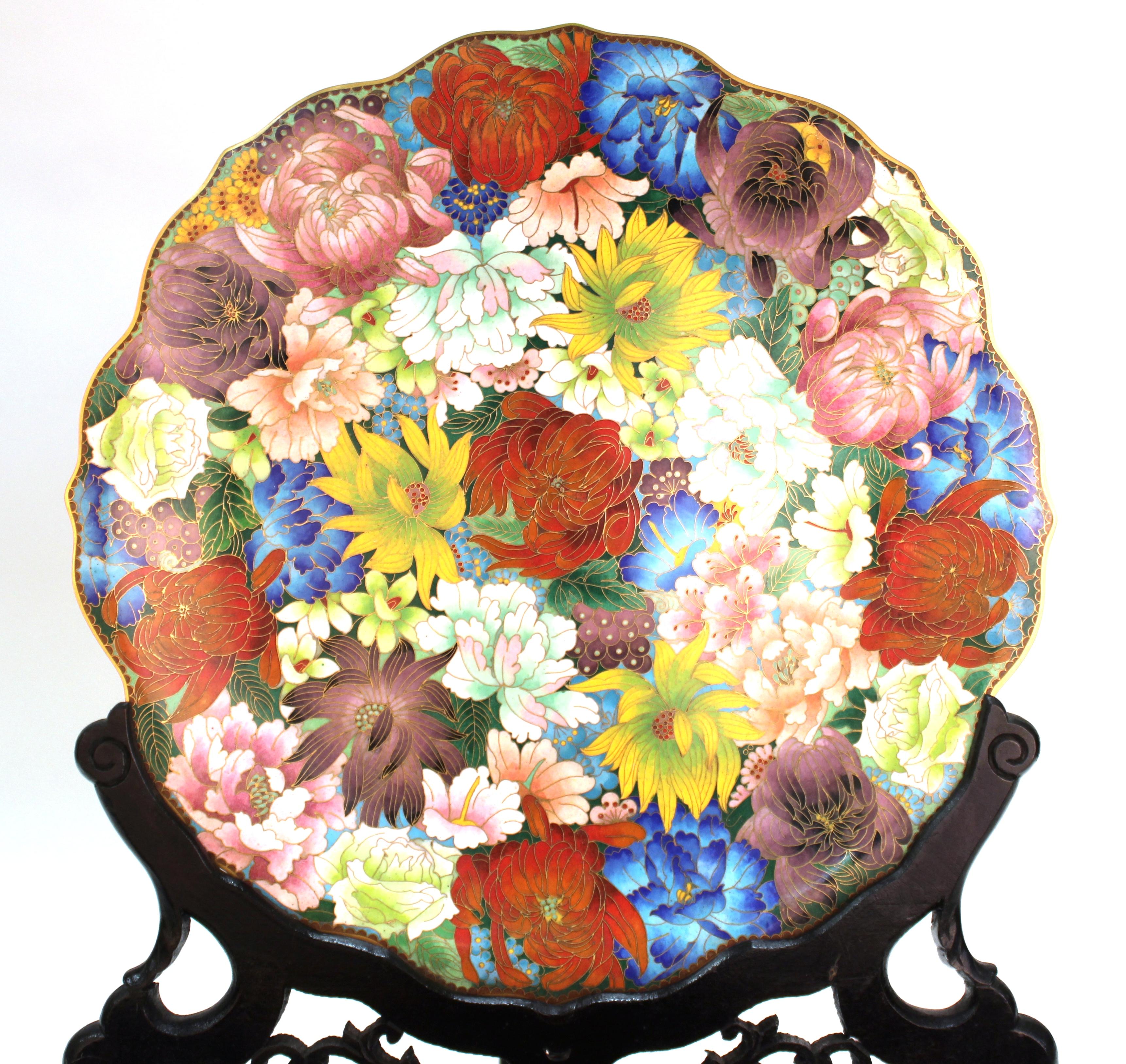 Chinese metal cloisonné charger with multicolored floral motif on the front face and a blue enamel back with stylized floral motif. The piece was made in circa 1930 and comes with a carved ebonized wooden stand.