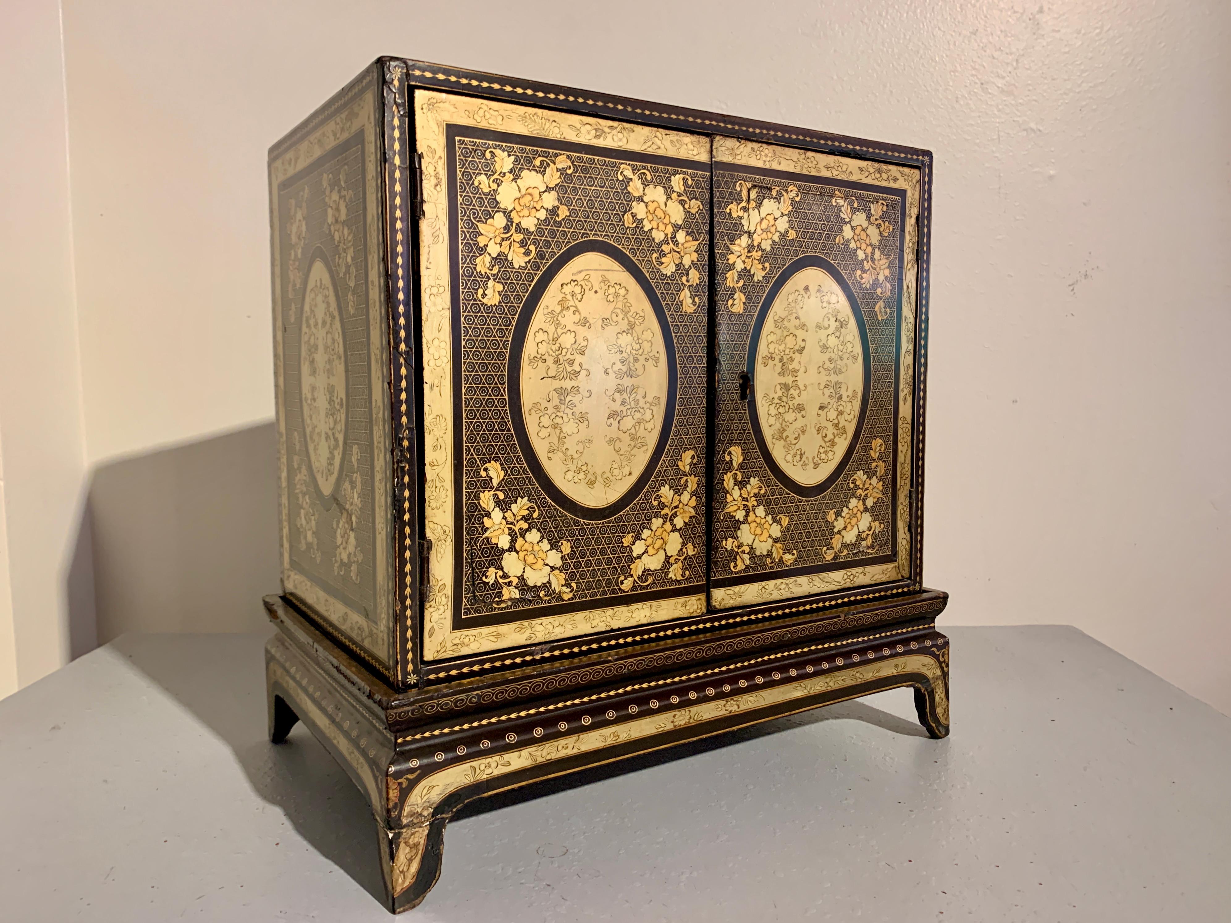 An exquisite small Chinese export cabinet on stand, black lacquer and gilt painted, early to mid 19th century, China. 

The small lacquer cabinet of black lacquer with stunning gilt painted designs of peonies against a meticulous geometric diaper