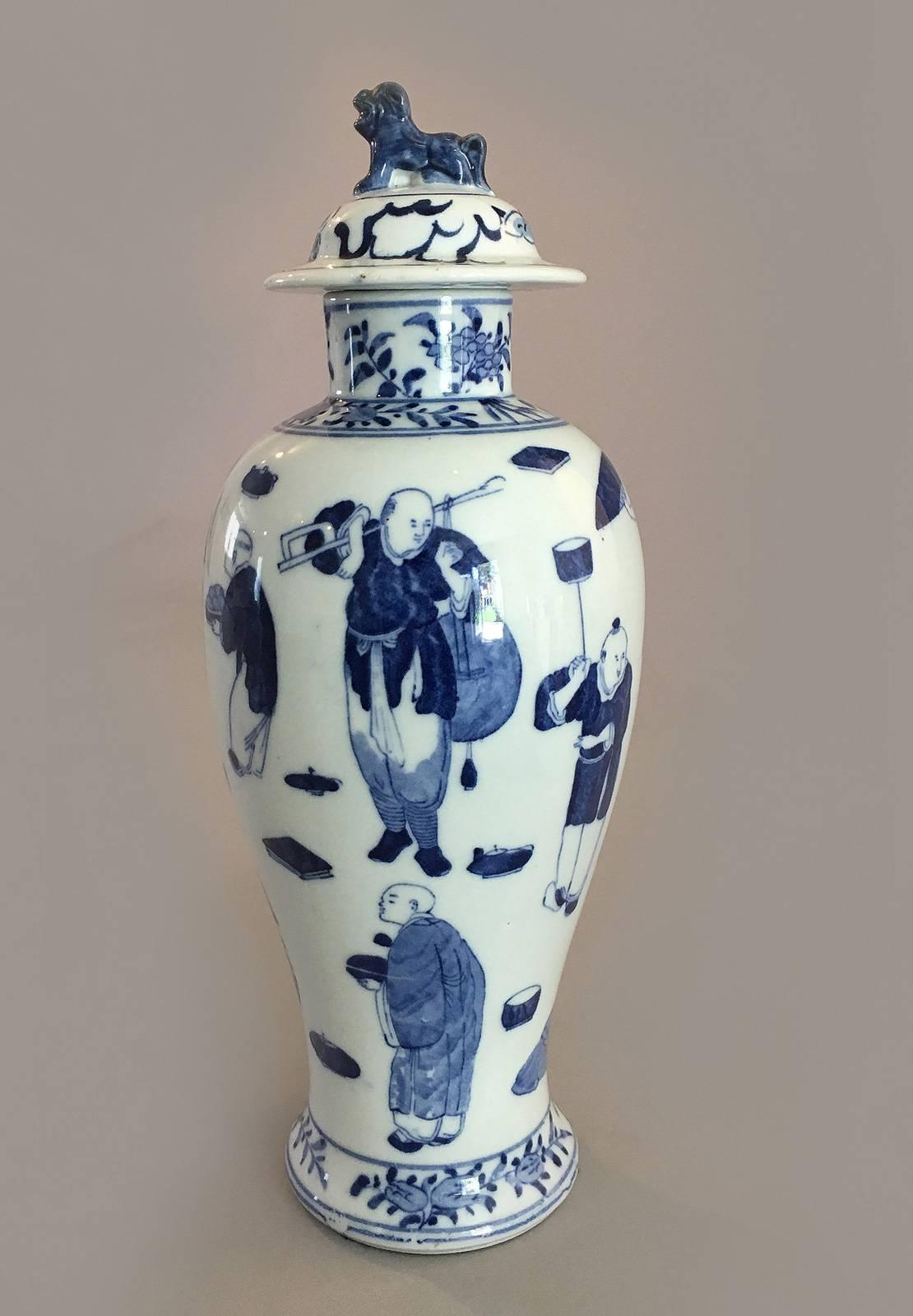 Chinese export porcelain blue and white baluster-shaped vase and cover with foo dog finial. It is decorated with male figures in various pursuits: one dancing holding a fan and sword, one holding the hand of a child, one carrying a stack of round