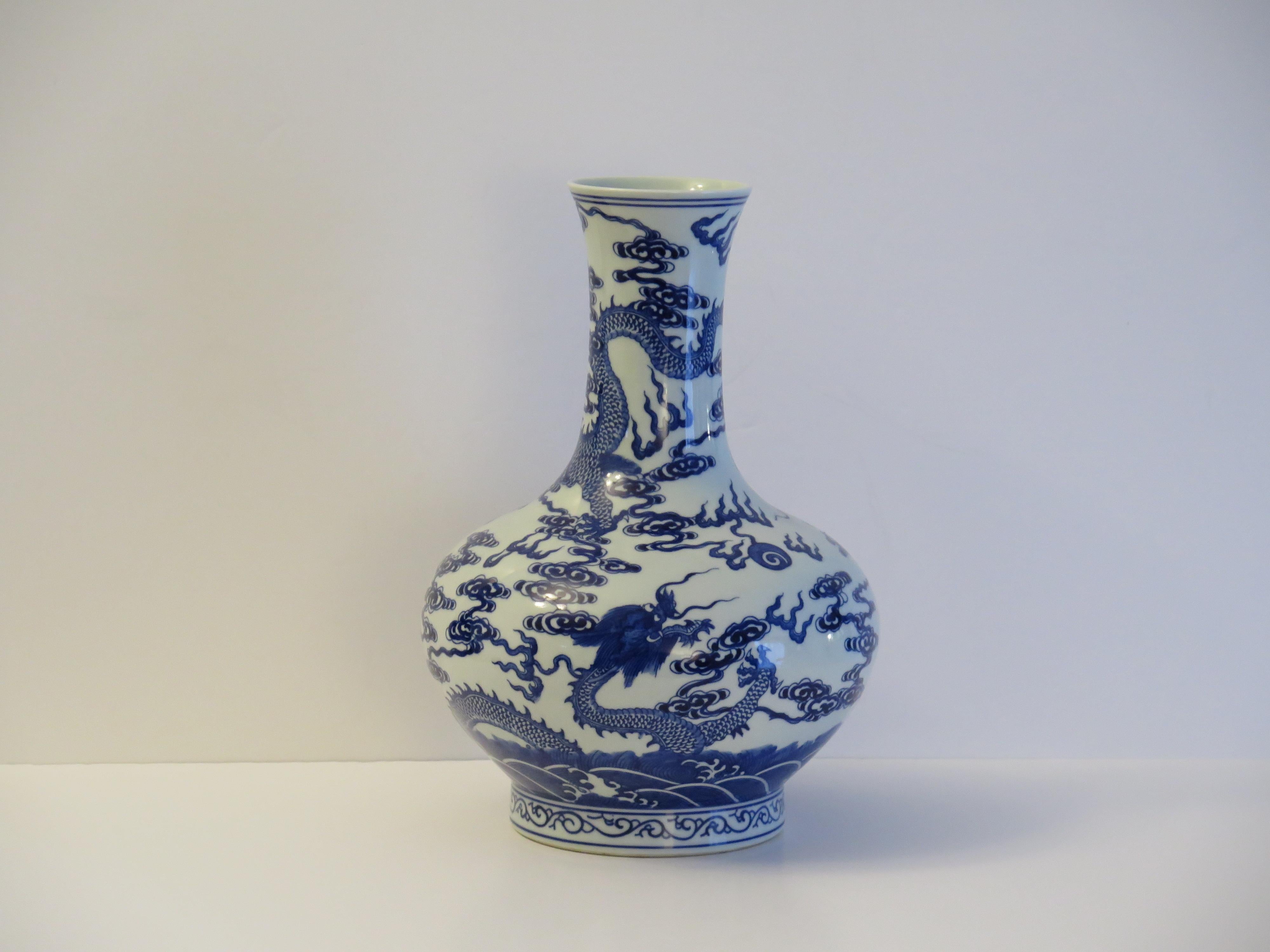 Es handelt sich um eine elegante Flaschenvase aus chinesischem Exportporzellan, die auf einem niedrigen Fuß steht und von Hand mit einem blau-weißen Drachenmuster bemalt ist. Sie stammt aus der Mitte des 20. Jahrhunderts, etwa aus den 1950er