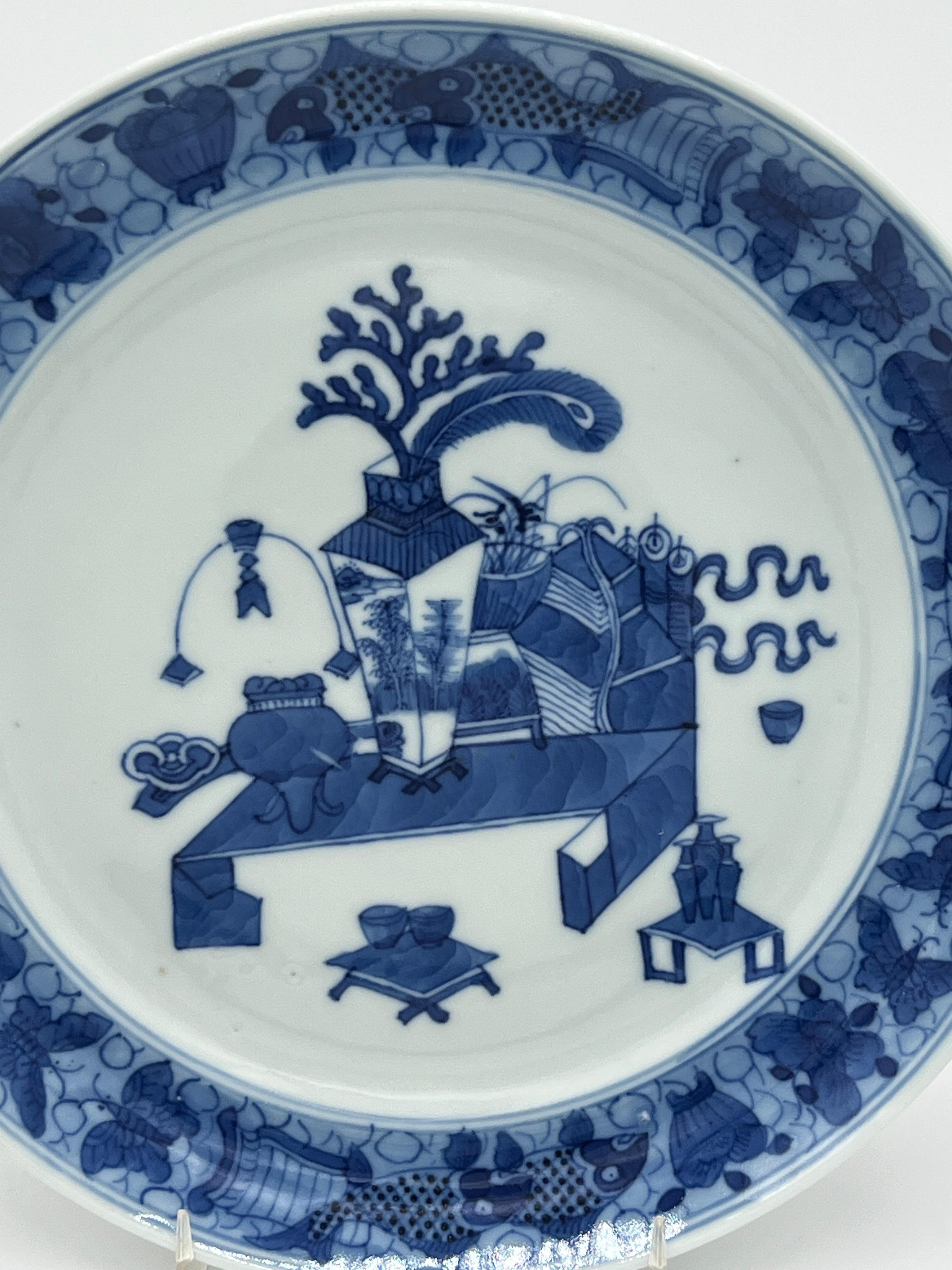 Chinese, circa 1780.

Chinese export blue & white plate, painted with a ‘precious objects’, pattern, with scrolls, censors & teawares, within a border of fish and moths on a scale ground. Unmarked, c.1780