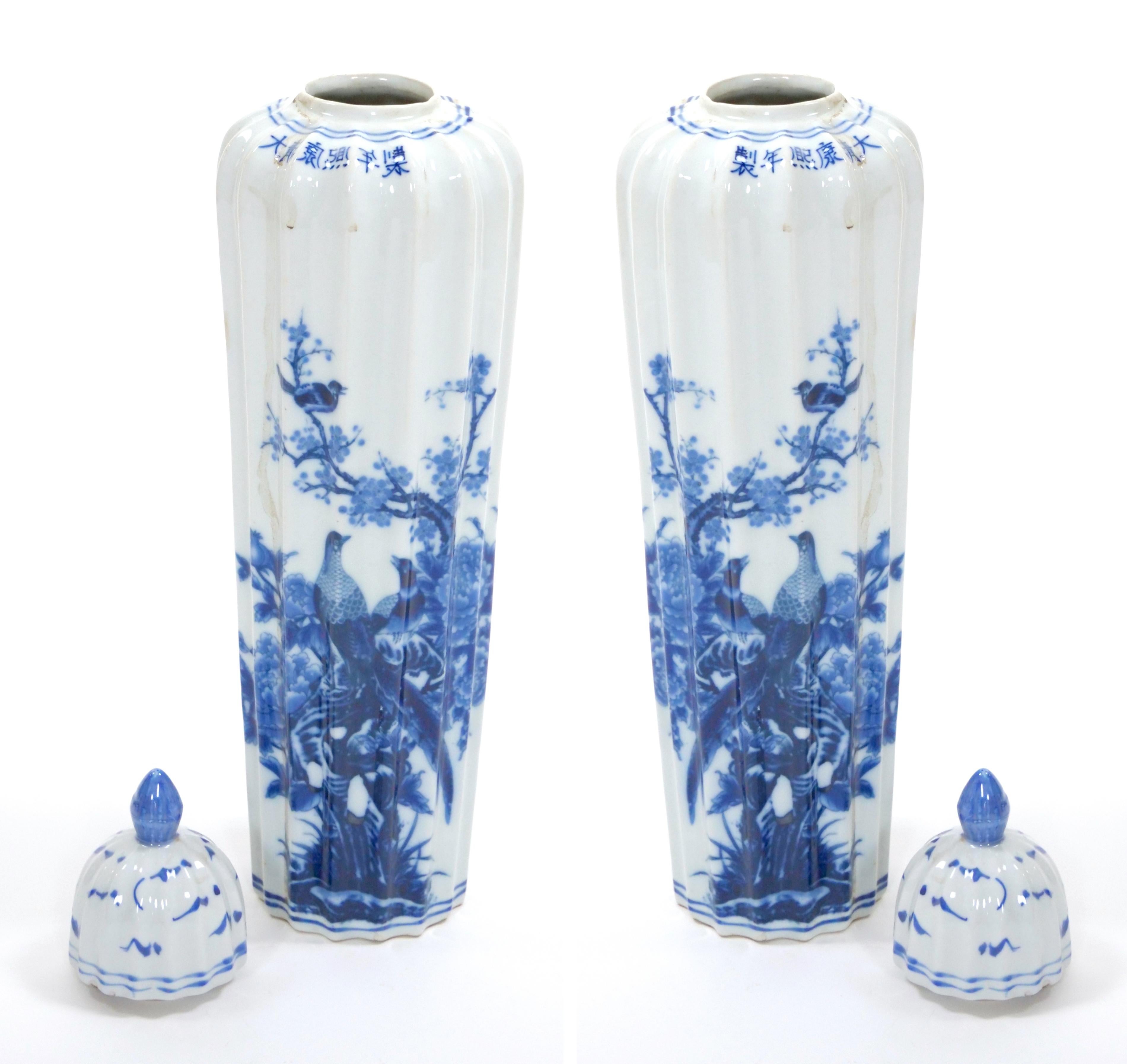 Presenting a stunning pair of 19th century Chinese Export Blue and White Porcelain Tall Covered Decorative Urns. These exceptional urns showcase a timeless aesthetic with their intricate hand-painted floral and foliate designs, featuring birds and