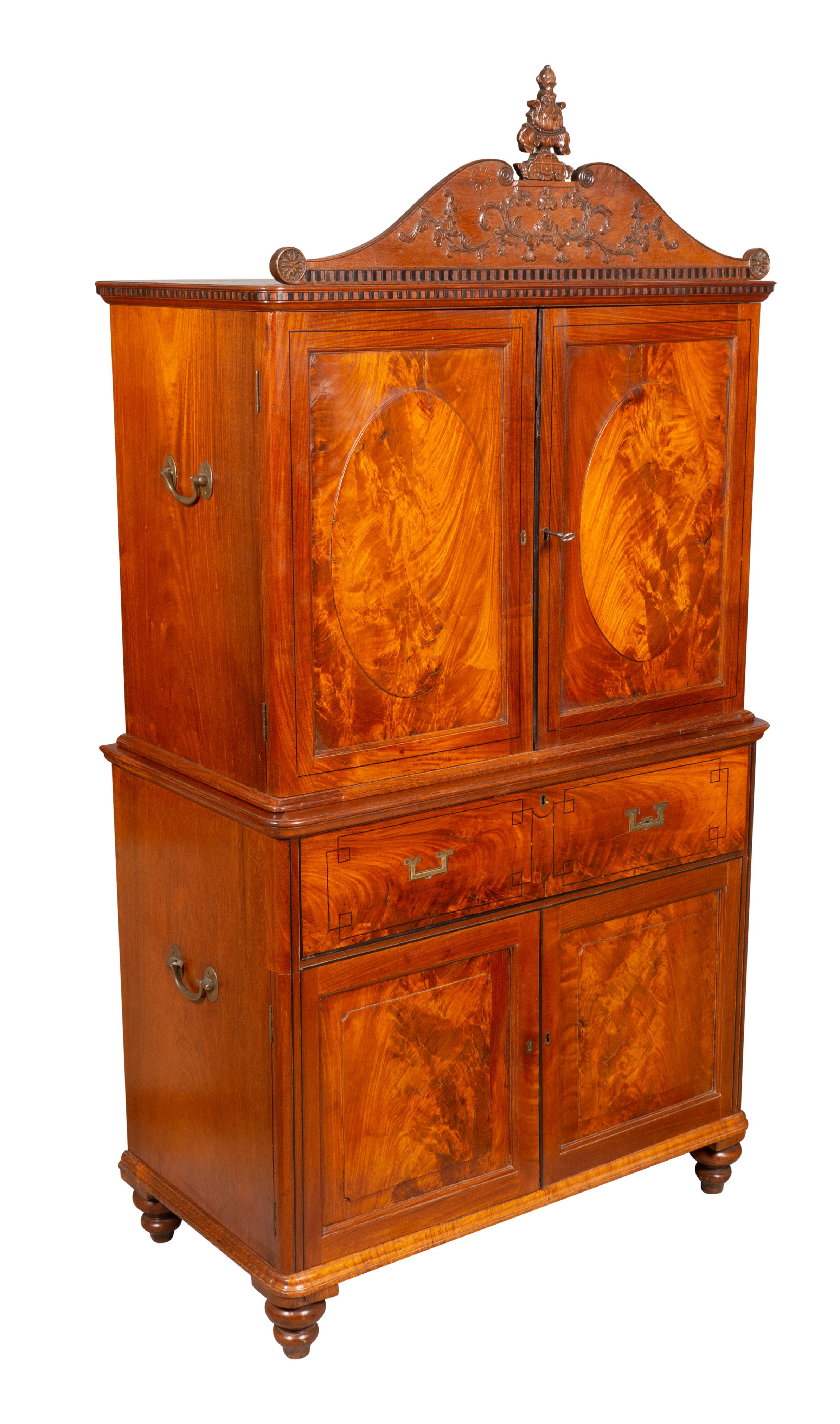 An unusual cabinet commissioned in China by a British officer. In two parts for transporting. Of diminutive scale with a removable carved cornice seated on a cabinet with two paneled doors opening to slide out linen drawers. The base with a top