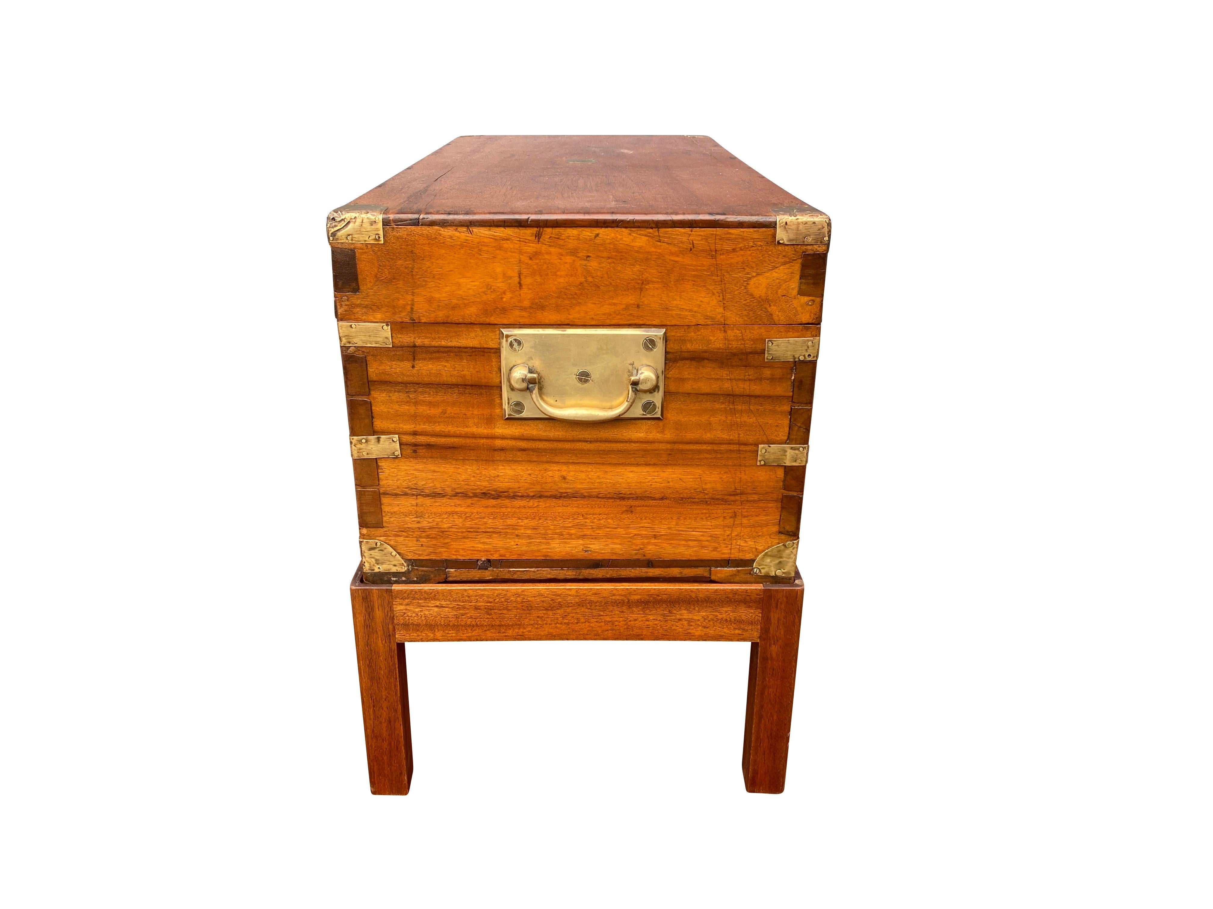 Rectangular hinged top with brass corners and central small plaque over a conforming case set in a later base with square section legs. Brass side handles.