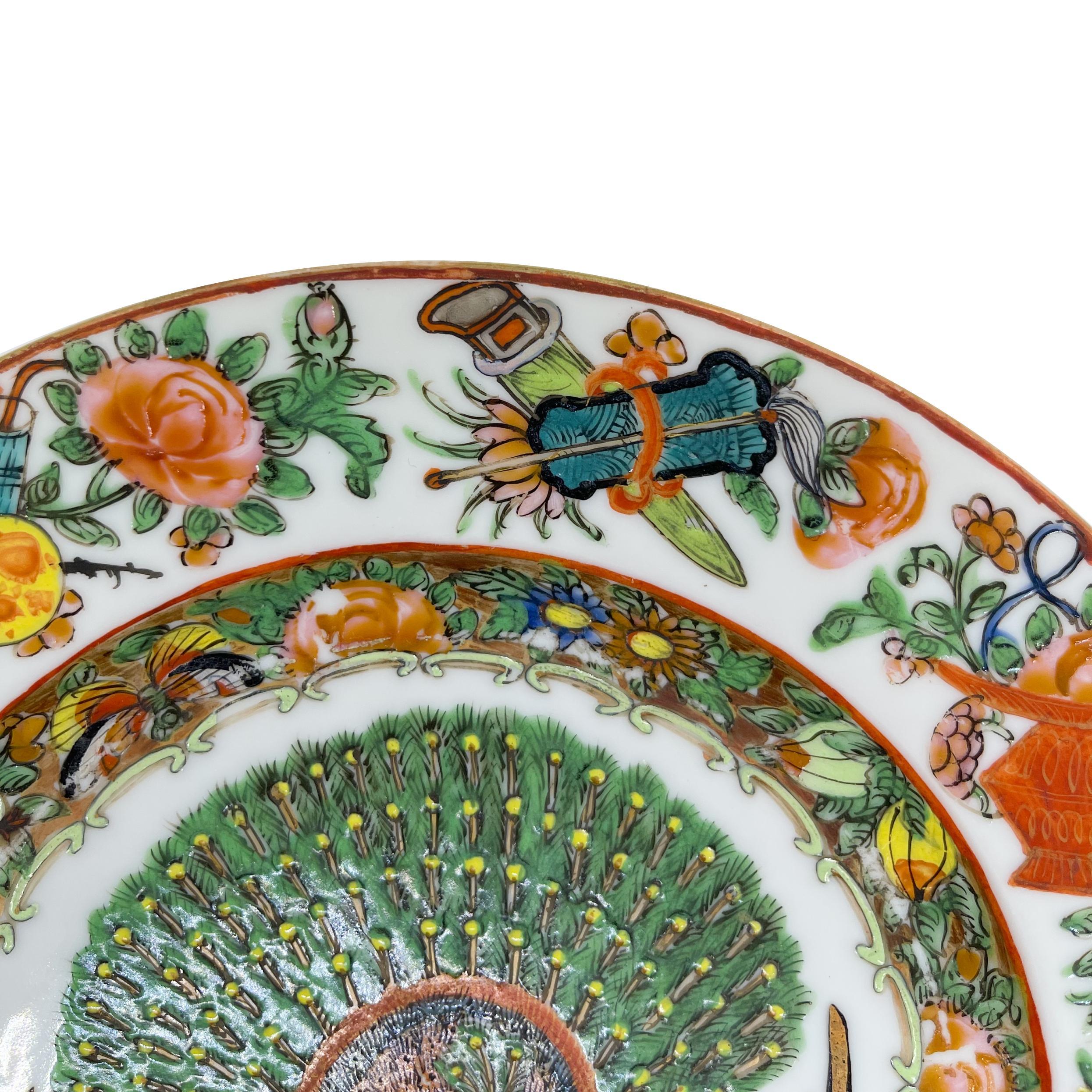 Assiette rose de la famille de Canton, dynastie Qing, époque Tongzhi, vers 1865. 
Le rondeau central est orné d'un paon en émail polychrome, la bordure intérieure du cavet est ornée d'un motif floral et fruitier avec deux papillons sur fond doré,