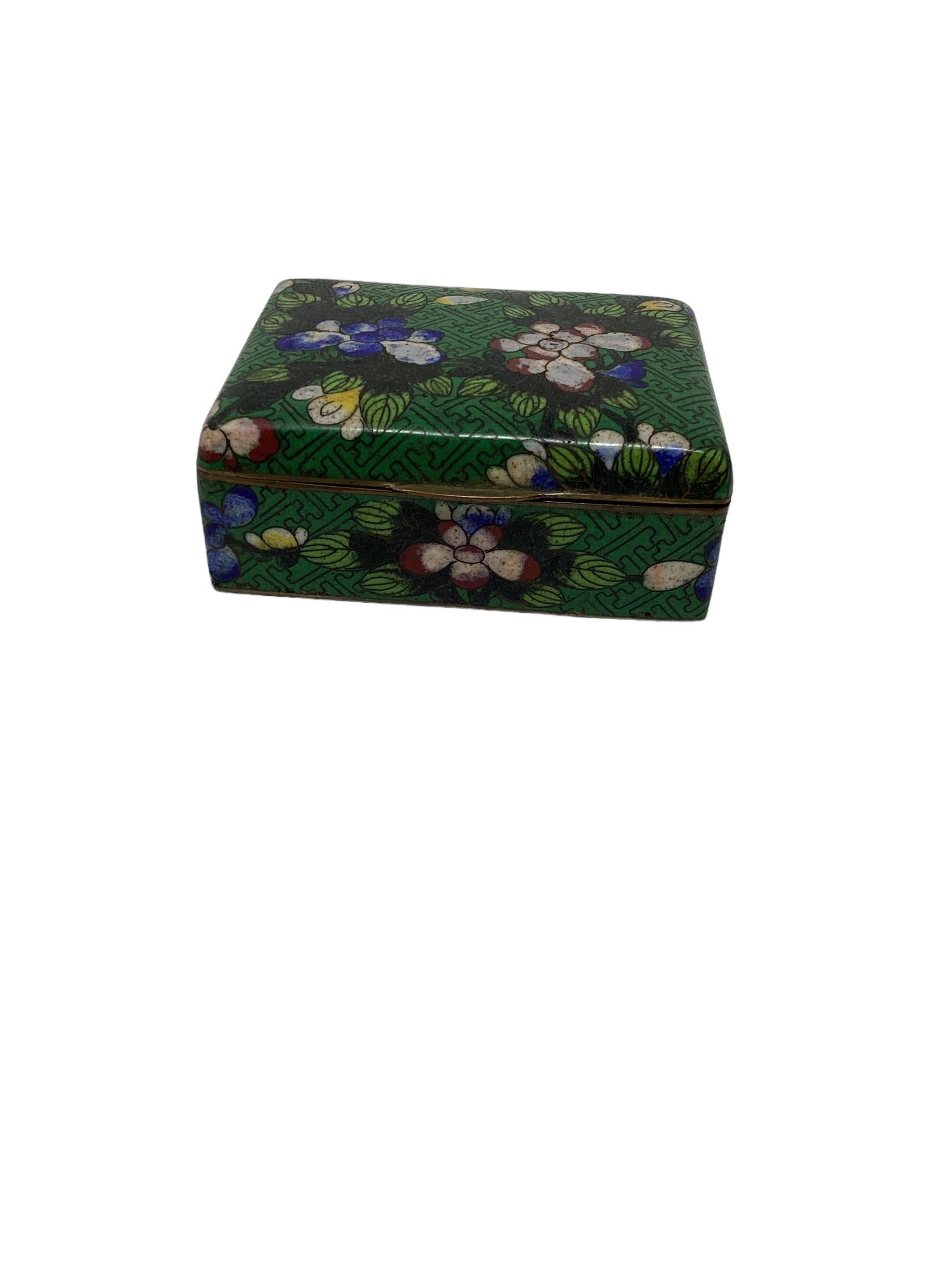Lovely Chinese export cloisonné box made of brass and enameled with a beautiful floral pattern on a green background. This decorative box was most likely a cigarette box or trinket box and would make a great desk accessory or cocktail table